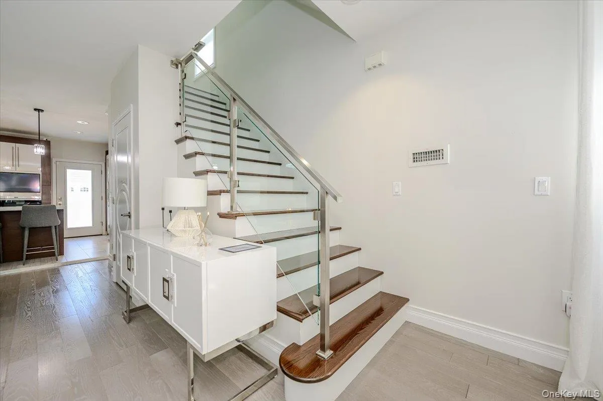 Modern staircase featuring horizontal metal railings, wood-finish treads, and a white painted base with integrated storage cabinetry Modern staircase featuring horizontal metal railings, wood-finish treads, and a white painted base with integrated storage cabinetry