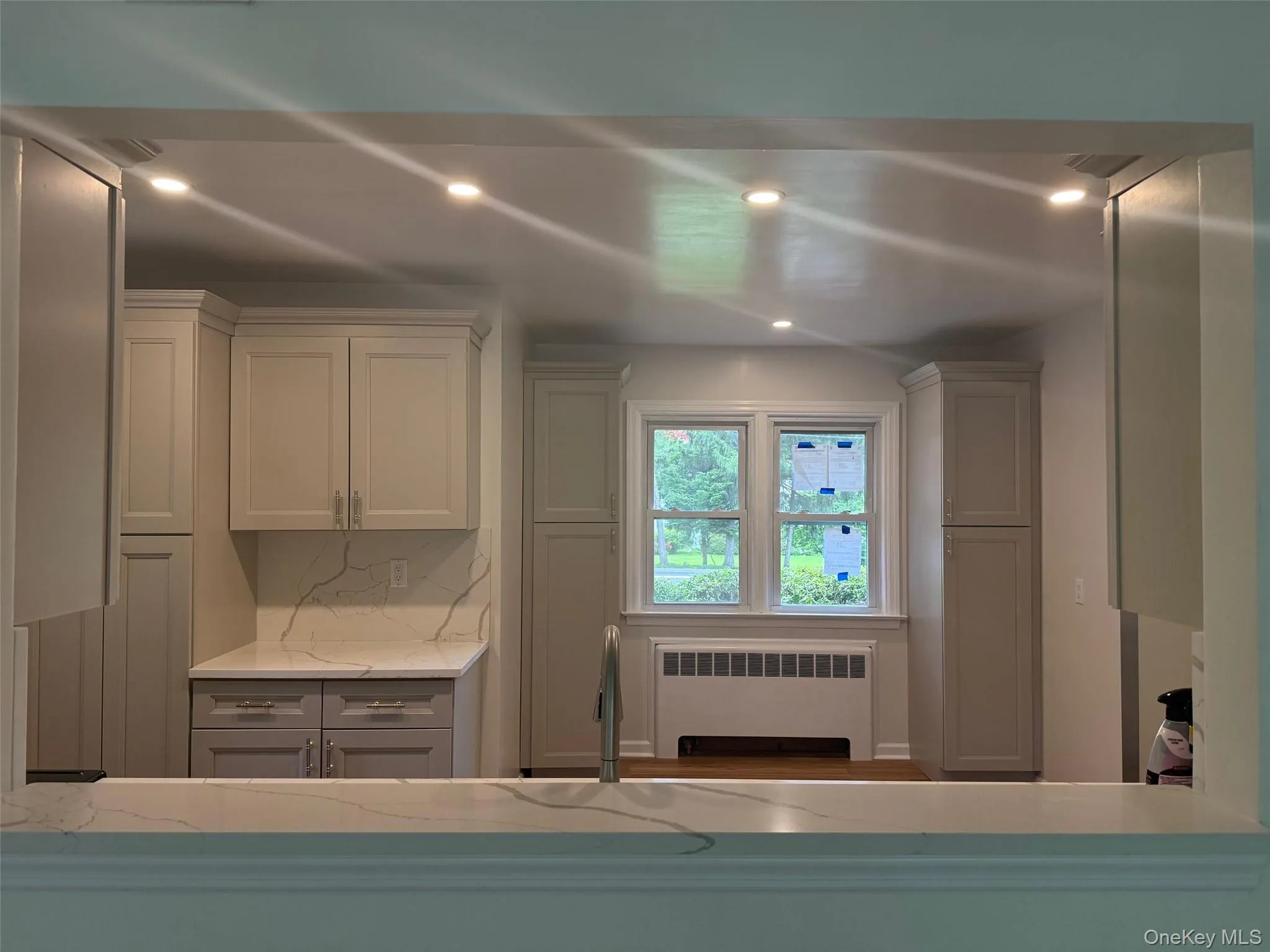 Kitchen featuring radiator, recessed lighting, light stone countertops, tasteful backsplash, and white cabinetry Kitchen featuring radiator, recessed lighting, light stone countertops, tasteful backsplash, and white cabinetry