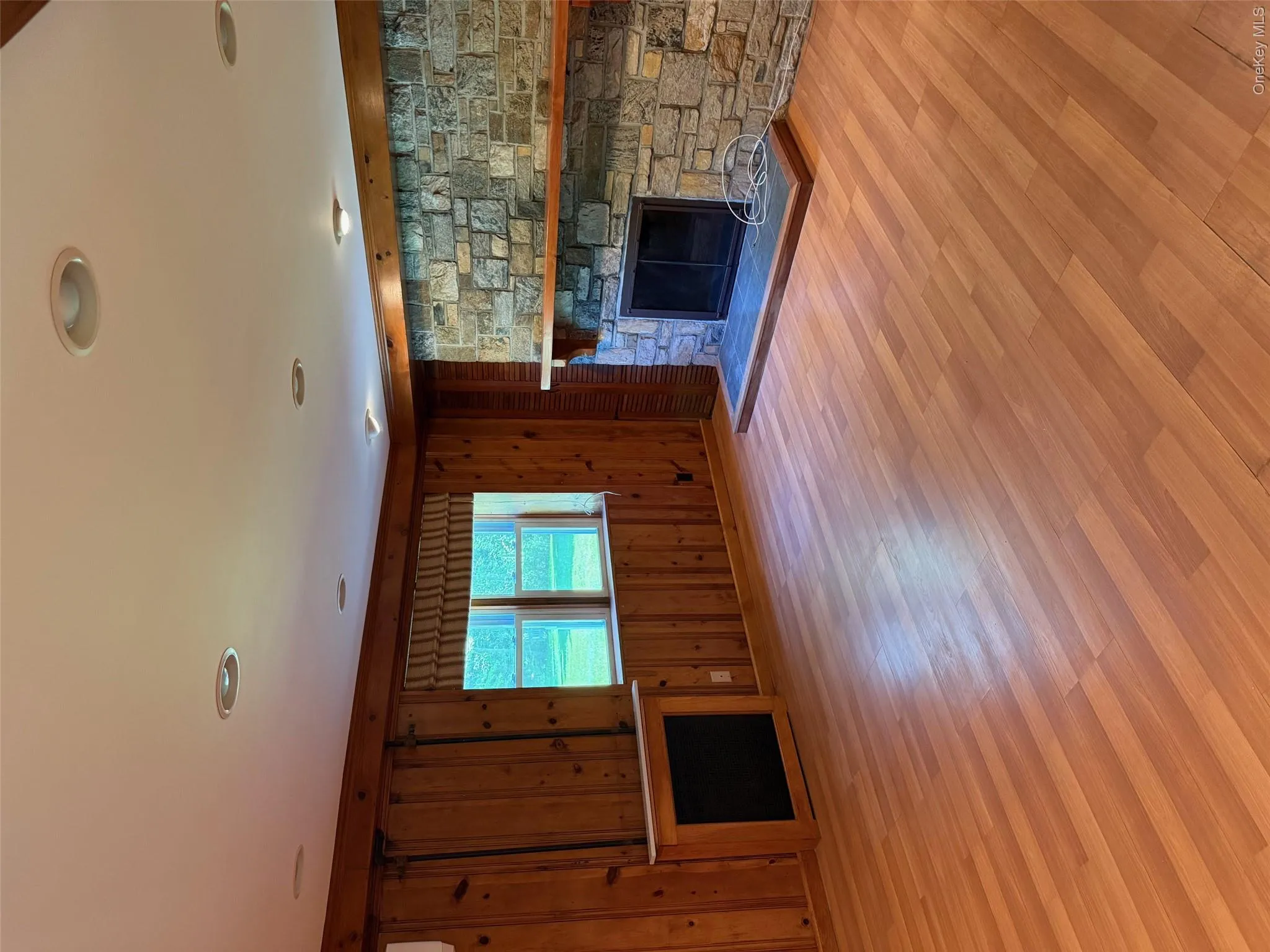 Unfurnished living room with a stone fireplace, wood finished floors, and wooden walls Unfurnished living room with a stone fireplace, wood finished floors, and wooden walls
