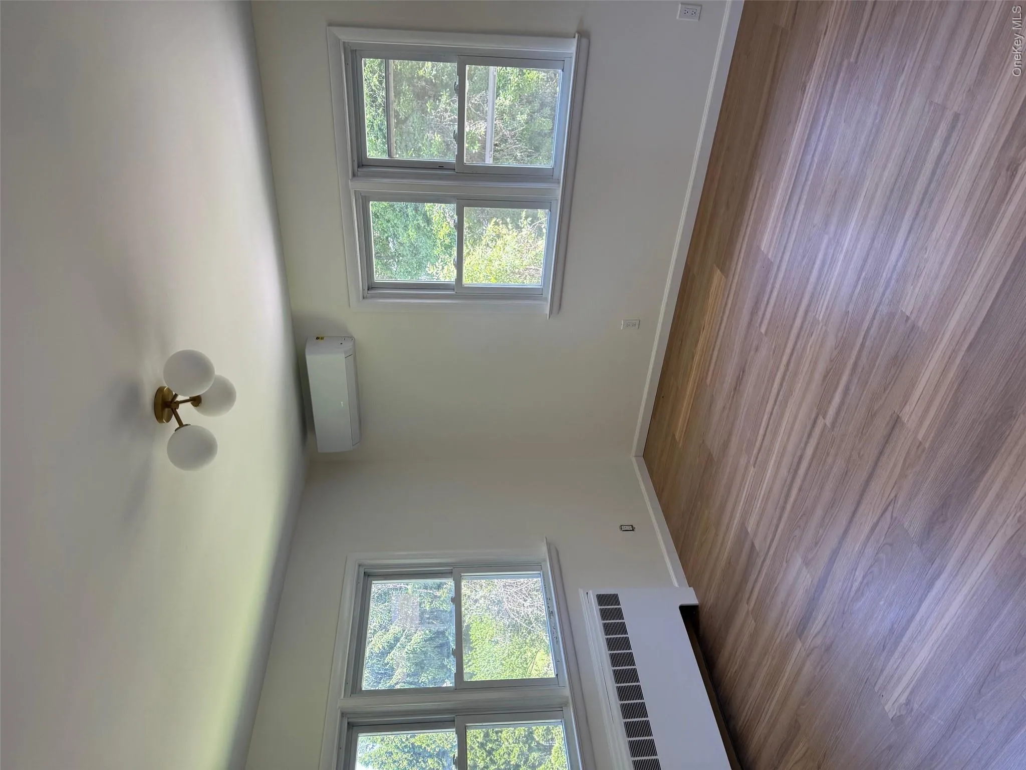 Unfurnished room featuring a wall mounted AC, radiator, wood finished floors, and baseboards Unfurnished room featuring a wall mounted AC, radiator, wood finished floors, and baseboards