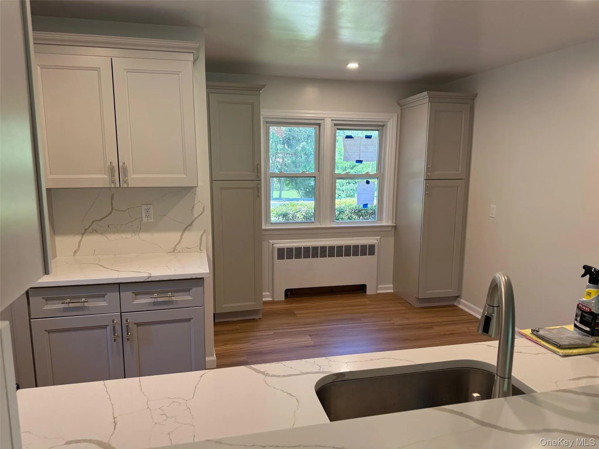 Kitchen with radiator, gray cabinetry, a sink, wood finished floors, and light stone countertops Kitchen with radiator, gray cabinetry, a sink, wood finished floors, and light stone countertops
