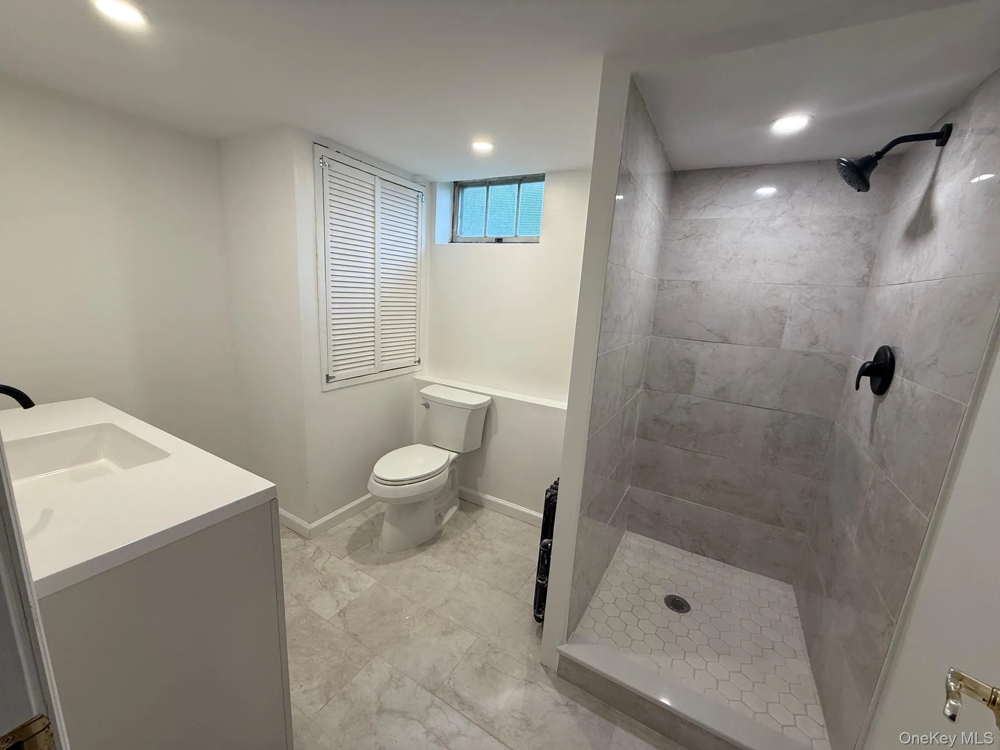 Full bathroom with toilet, a tile shower, vanity, baseboards, and recessed lighting Full bathroom with toilet, a tile shower, vanity, baseboards, and recessed lighting