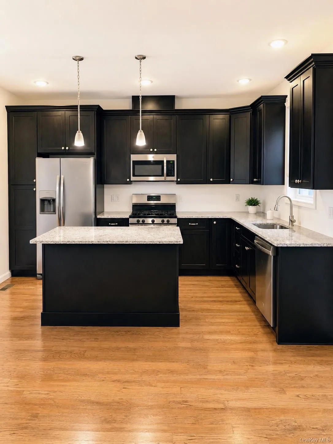 Kitchen with dark cabinetry, stainless steel appliances, a center island with a light-toned countertop, recessed lighting, and wood-finish flooring Kitchen with dark cabinetry, stainless steel appliances, a center island with a light-toned countertop, recessed lighting, and wood-finish flooring