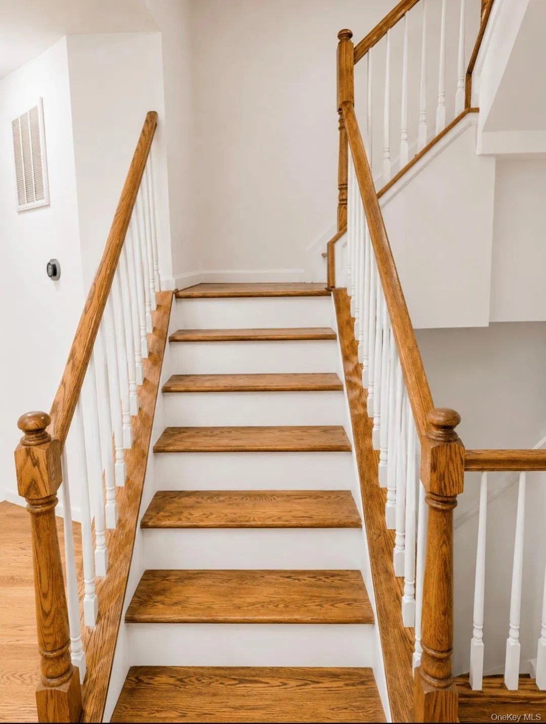 Staircase with wood-finish treads and white risers, featuring a wood-finish handrail and white balusters Staircase with wood-finish treads and white risers, featuring a wood-finish handrail and white balusters