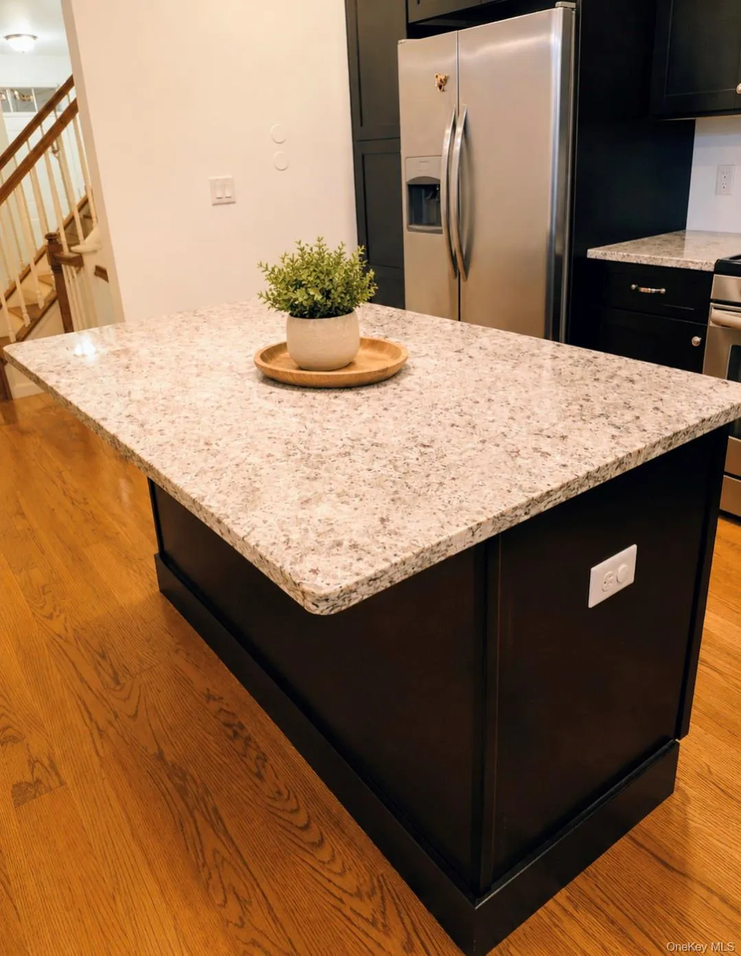 Kitchen island with a light-toned countertop, dark base cabinetry, and wood-finish flooring Kitchen island with a light-toned countertop, dark base cabinetry, and wood-finish flooring