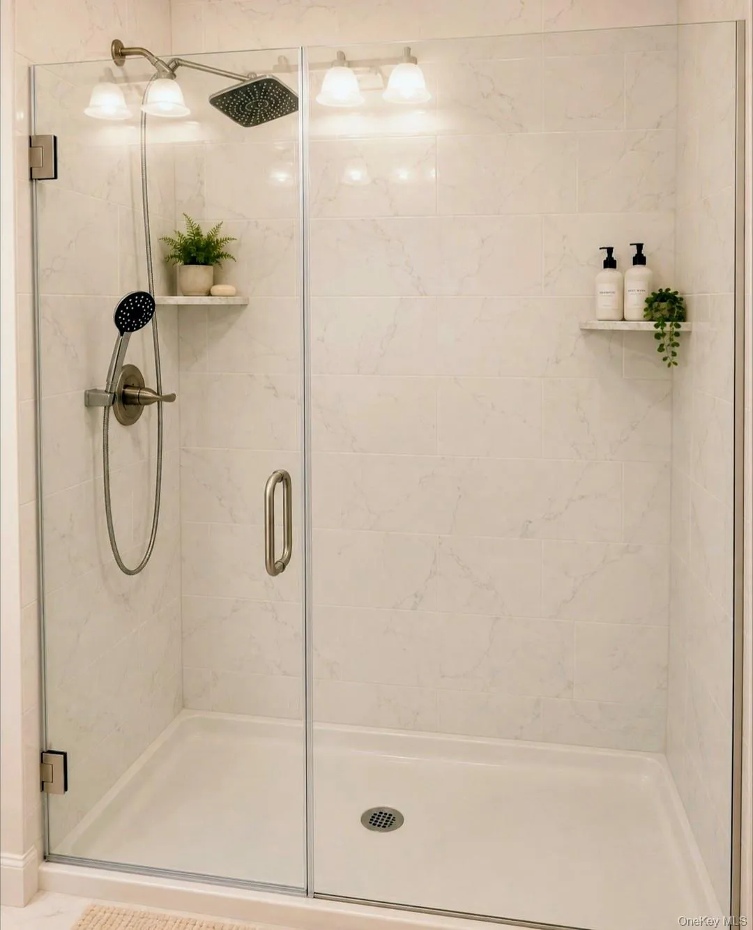 Glass-enclosed shower with a rainfall showerhead, handheld shower fixture, built-in recessed shelving, and tiled walls Glass-enclosed shower with a rainfall showerhead, handheld shower fixture, built-in recessed shelving, and tiled walls