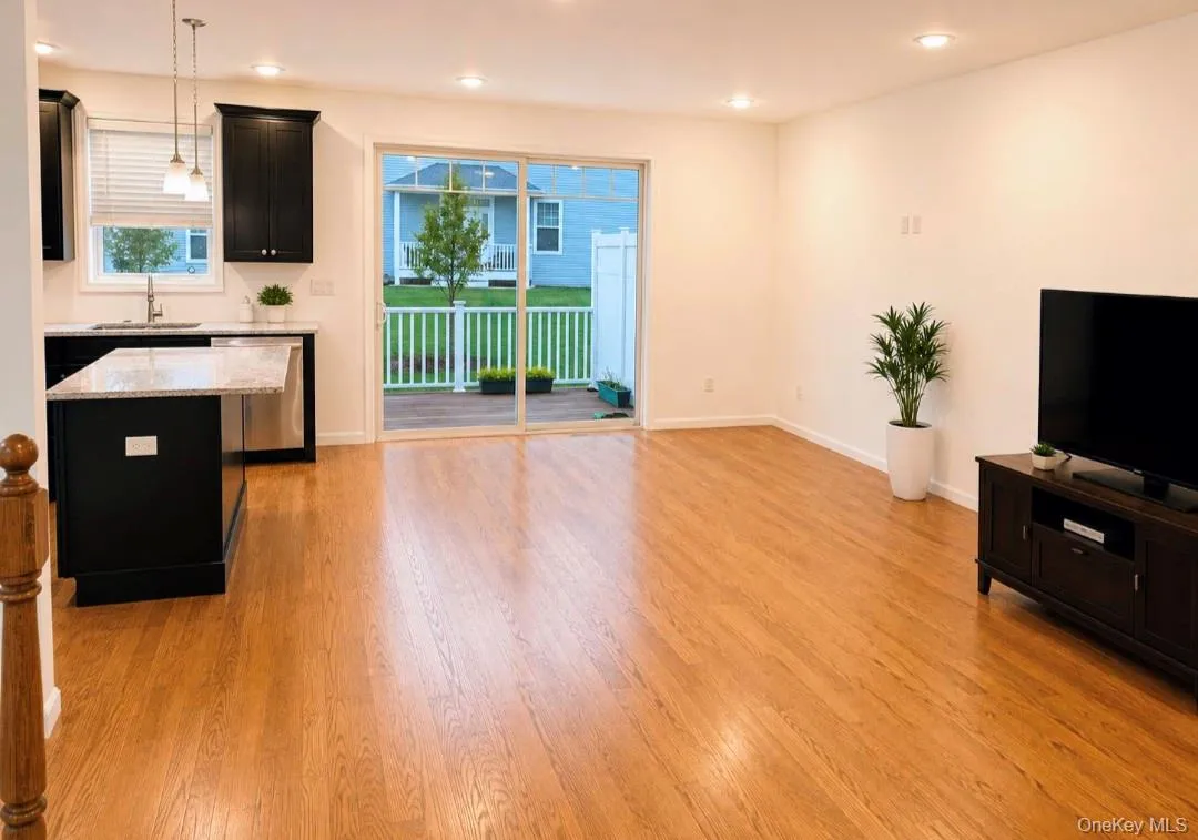 Hardwood flooring throughout living room, kitchen island with stone countertop, stainless steel appliances, recessed lighting, and sliding glass door leading to an outdoor deck Hardwood flooring throughout living room, kitchen island with stone countertop, stainless steel appliances, recessed lighting, and sliding glass door leading to an outdoor deck