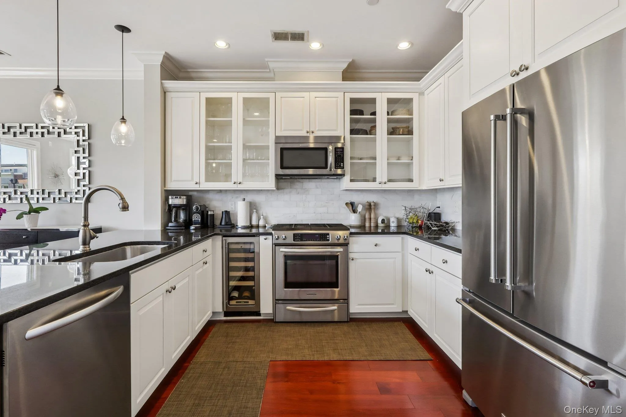 Kitchen featuring stainless steel appliances, white cabinetry, dark countertops, a tile backsplash, and mahogany wood flooring Kitchen featuring stainless steel appliances, white cabinetry, dark countertops, a tile backsplash, and mahogany wood flooring