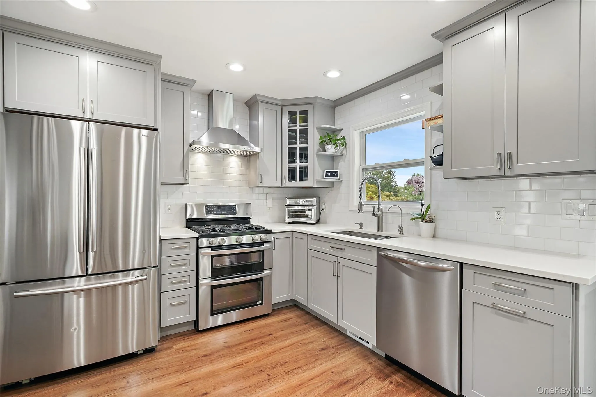 Recessed lighting, wood-finish flooring, light gray cabinetry, stainless steel appliances, and quartz countertops Recessed lighting, wood-finish flooring, light gray cabinetry, stainless steel appliances, and quartz countertops