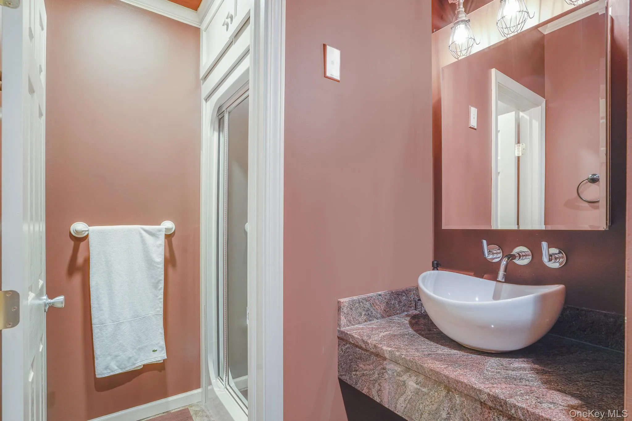 Vessel sink with wall-mounted faucet, granite-patterned countertop, and framed mirror with integrated lighting. Vessel sink with wall-mounted faucet, granite-patterned countertop, and framed mirror with integrated lighting.