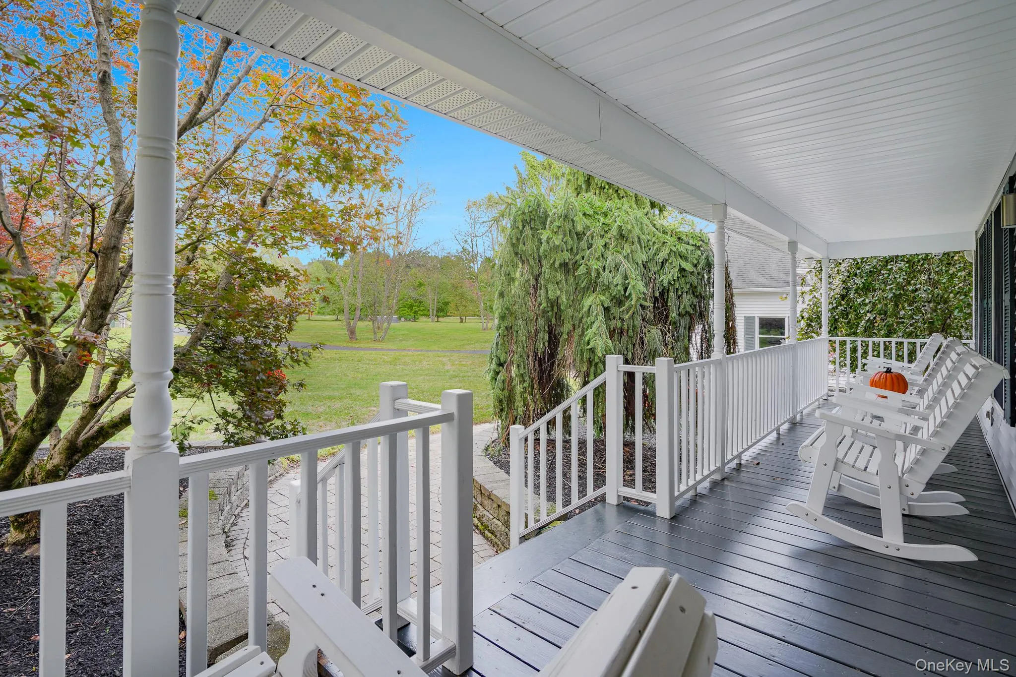 Expansive covered porch with white railings, a dark-stained wood-finish floor, and a beadboard ceiling. Expansive covered porch with white railings, a dark-stained wood-finish floor, and a beadboard ceiling.