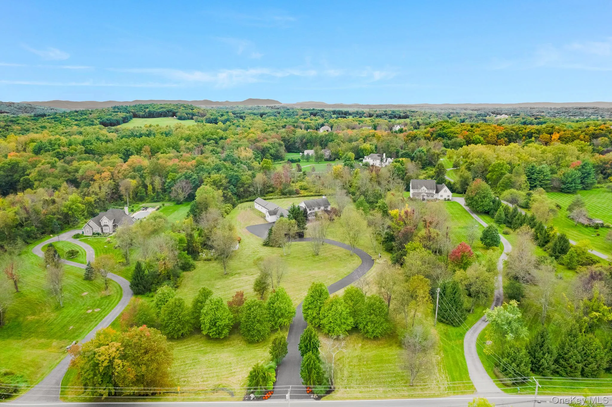 Expansive property featuring lush green lawns, mature trees, winding paved driveways, and distant forested hills. Expansive property featuring lush green lawns, mature trees, winding paved driveways, and distant forested hills.