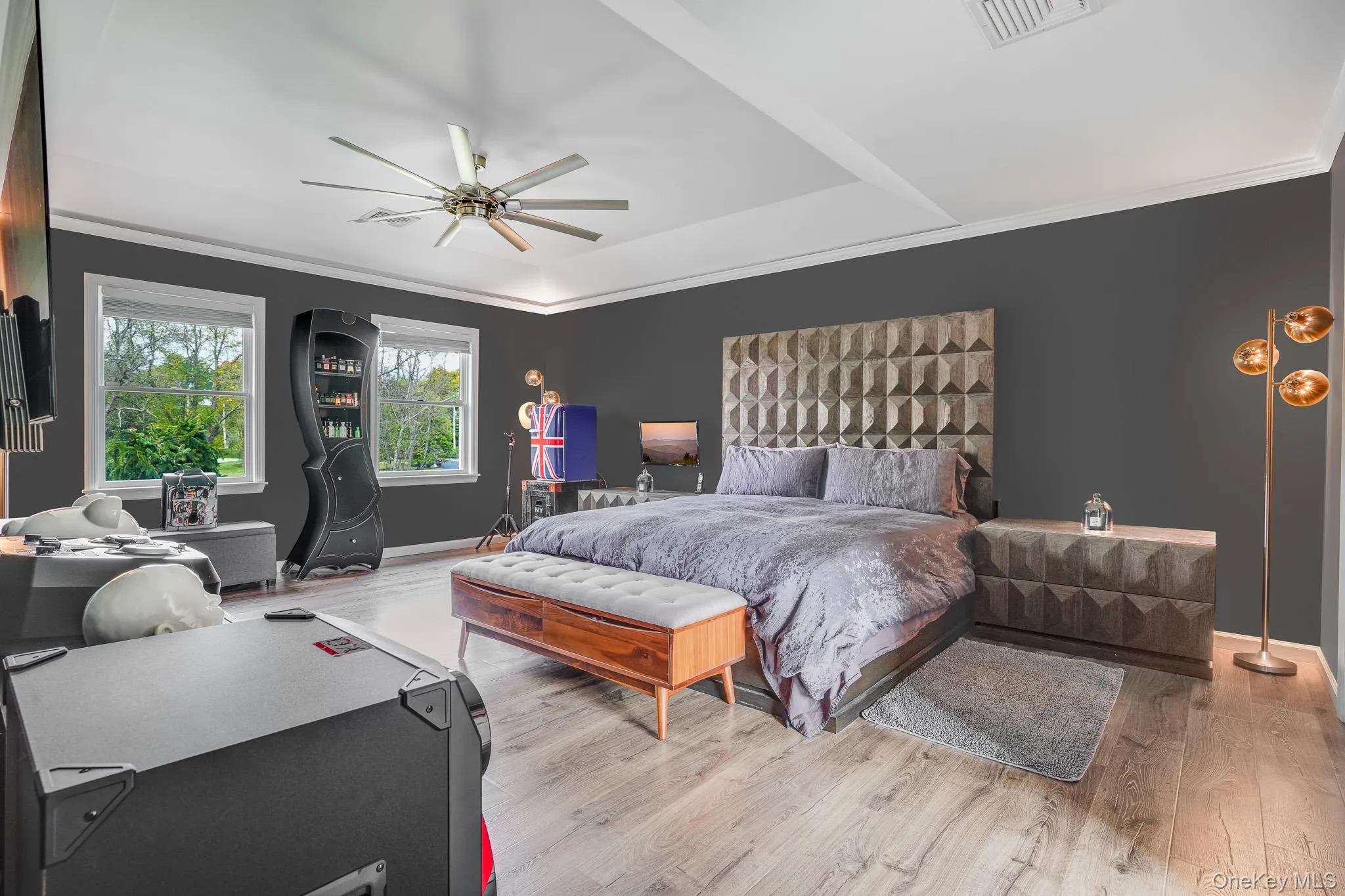 Tray ceiling with crown molding, light wood-finish flooring, multiple windows, and a large ceiling fan. Tray ceiling with crown molding, light wood-finish flooring, multiple windows, and a large ceiling fan.