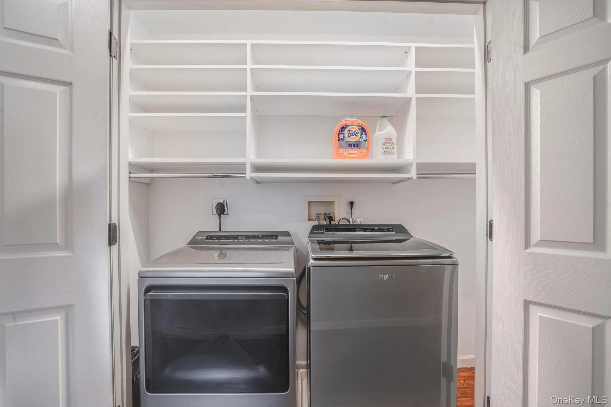 Laundry closet with white paneled doors, built-in shelving, and a hanging rod. Laundry closet with white paneled doors, built-in shelving, and a hanging rod.
