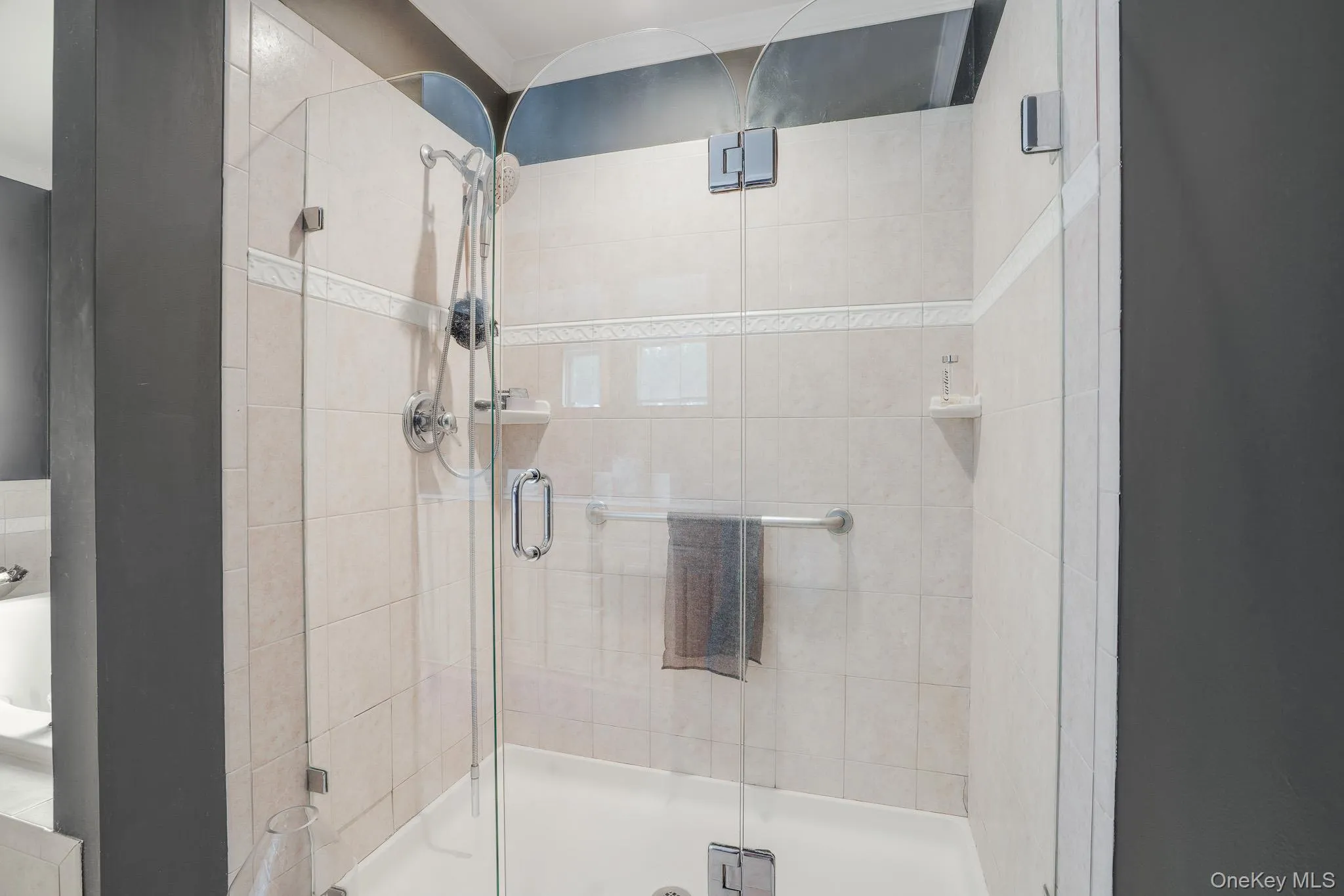 Frameless glass shower enclosure featuring a handheld showerhead, built-in soap dish, and a white shower pan. Frameless glass shower enclosure featuring a handheld showerhead, built-in soap dish, and a white shower pan.