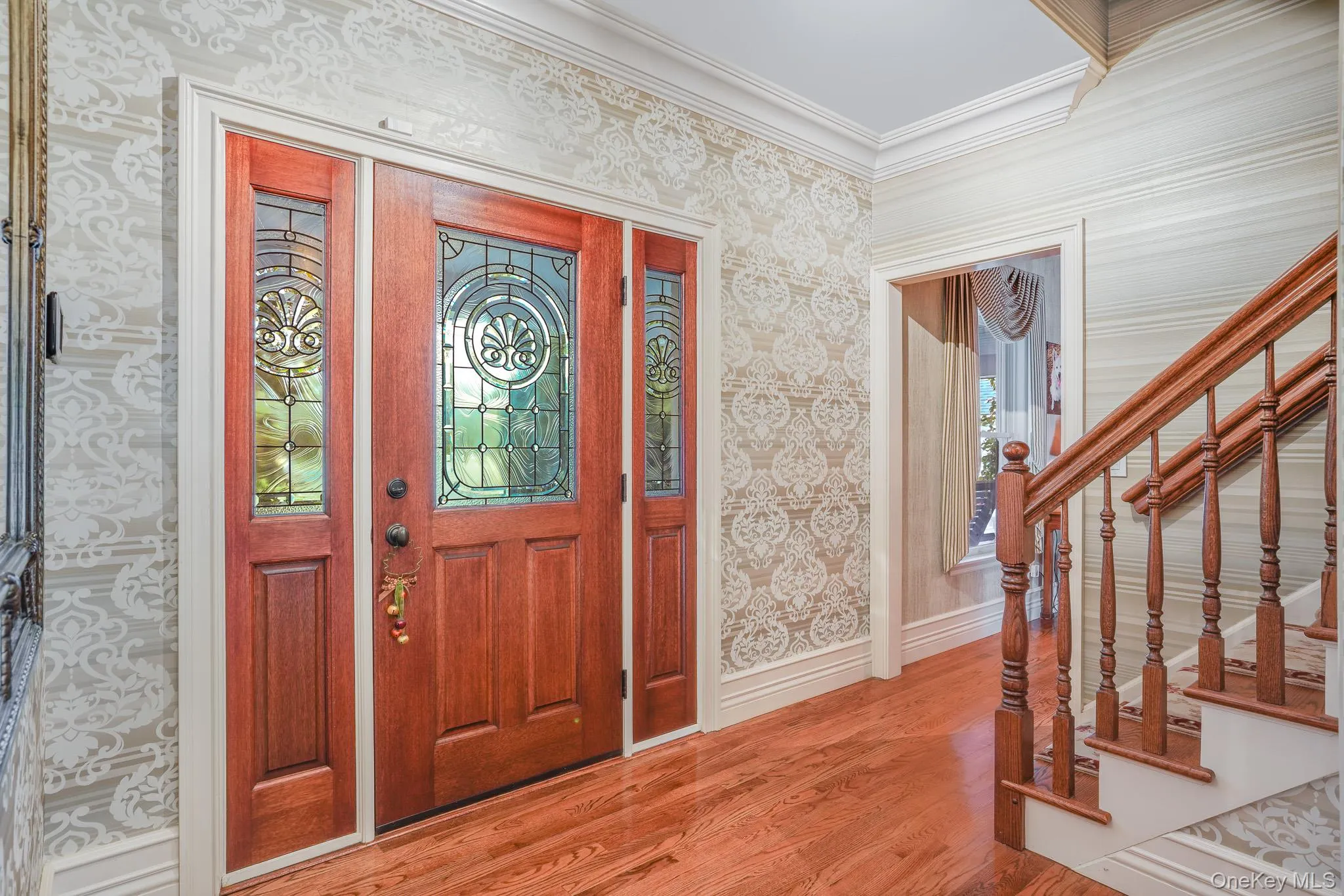 Hardwood flooring, decorative wallpaper, substantial wood staircase, crown molding, and a paneled entry door with leaded glass. Hardwood flooring, decorative wallpaper, substantial wood staircase, crown molding, and a paneled entry door with leaded glass.