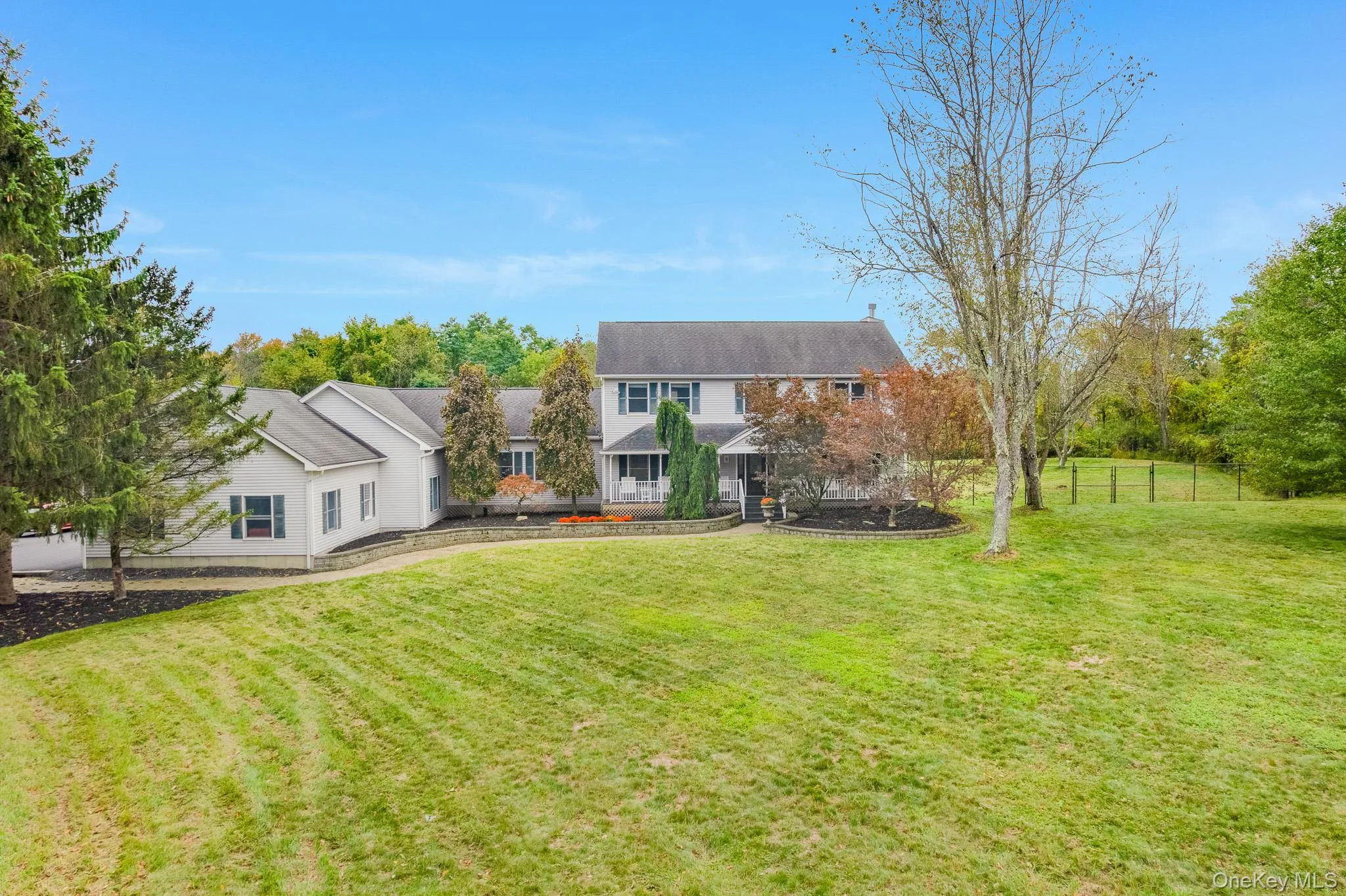 Expansive grassy lawn with established landscaping and mature trees and colonial style house with fencing. Expansive grassy lawn with established landscaping and mature trees and colonial style house with fencing.