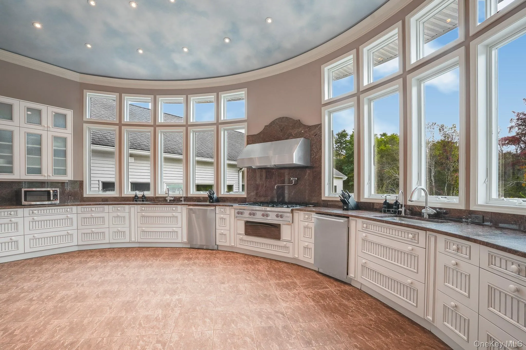 Curved chef's kitchen design featuring 20 foot windows on a rotunda wall, extensive white cabinetry, brown countertops, and stainless steel appliances. Curved chef's kitchen design featuring 20 foot windows on a rotunda wall, extensive white cabinetry, brown countertops, and stainless steel appliances.