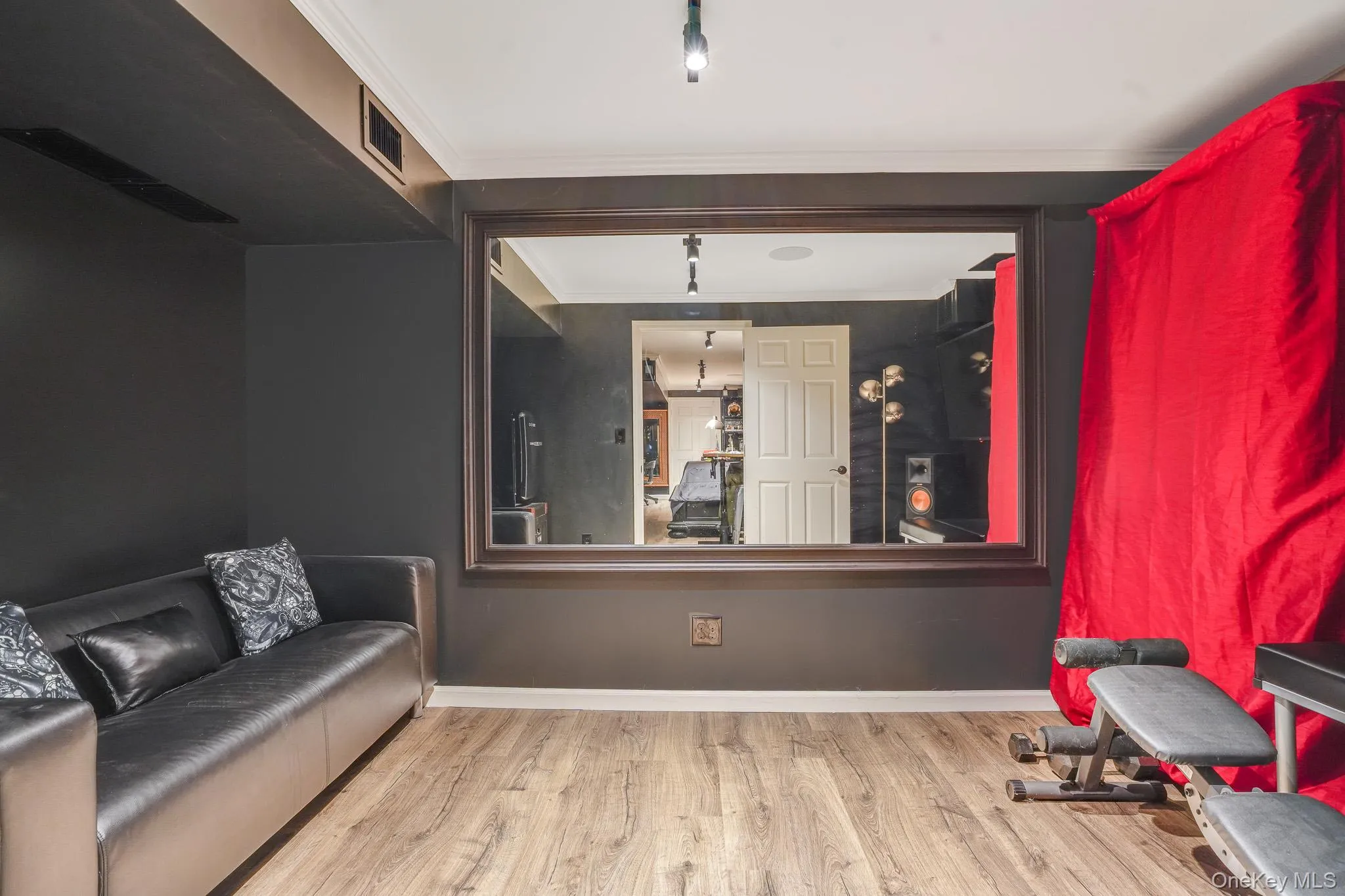 Basement room with wood-finish flooring, dark wall paint, and a large wall-mounted mirror Basement room with wood-finish flooring, dark wall paint, and a large wall-mounted mirror