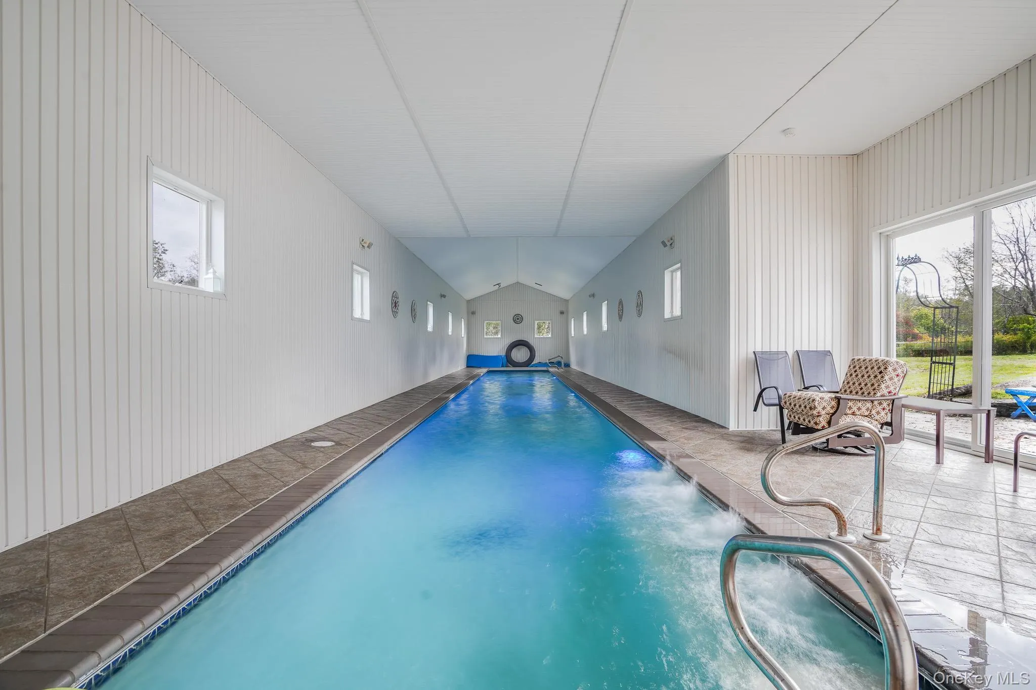 Indoor 75 foot lap pool with vaulted ceiling, multiple windows, tiled surround, and direct outdoor access Indoor 75 foot lap pool with vaulted ceiling, multiple windows, tiled surround, and direct outdoor access