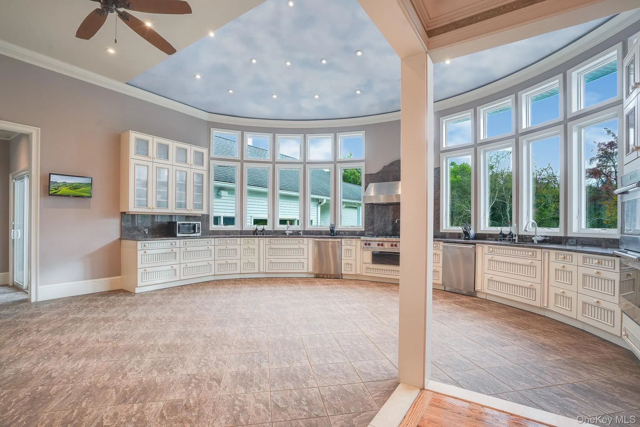 Curved chef's kitchen design featuring 20 foot windows on a rotunda wall, extensive white cabinetry, brown countertops, and stainless steel appliances. Curved chef's kitchen design featuring 20 foot windows on a rotunda wall, extensive white cabinetry, brown countertops, and stainless steel appliances.
