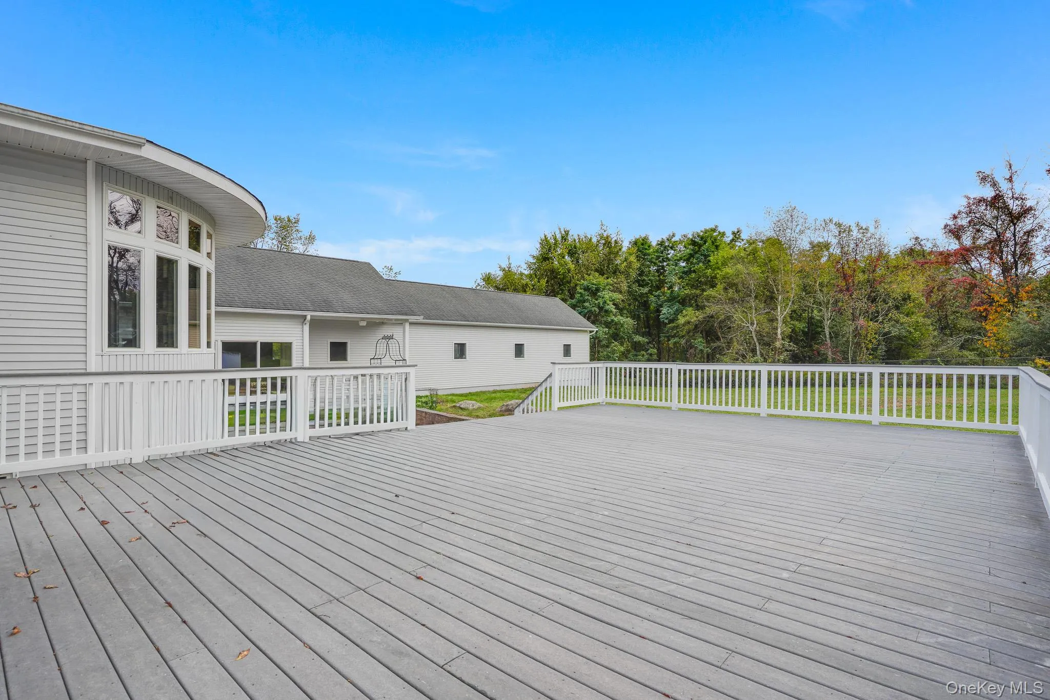 Expansive composite deck with white railings, featuring a curved bay window and siding exterior. Expansive composite deck with white railings, featuring a curved bay window and siding exterior.