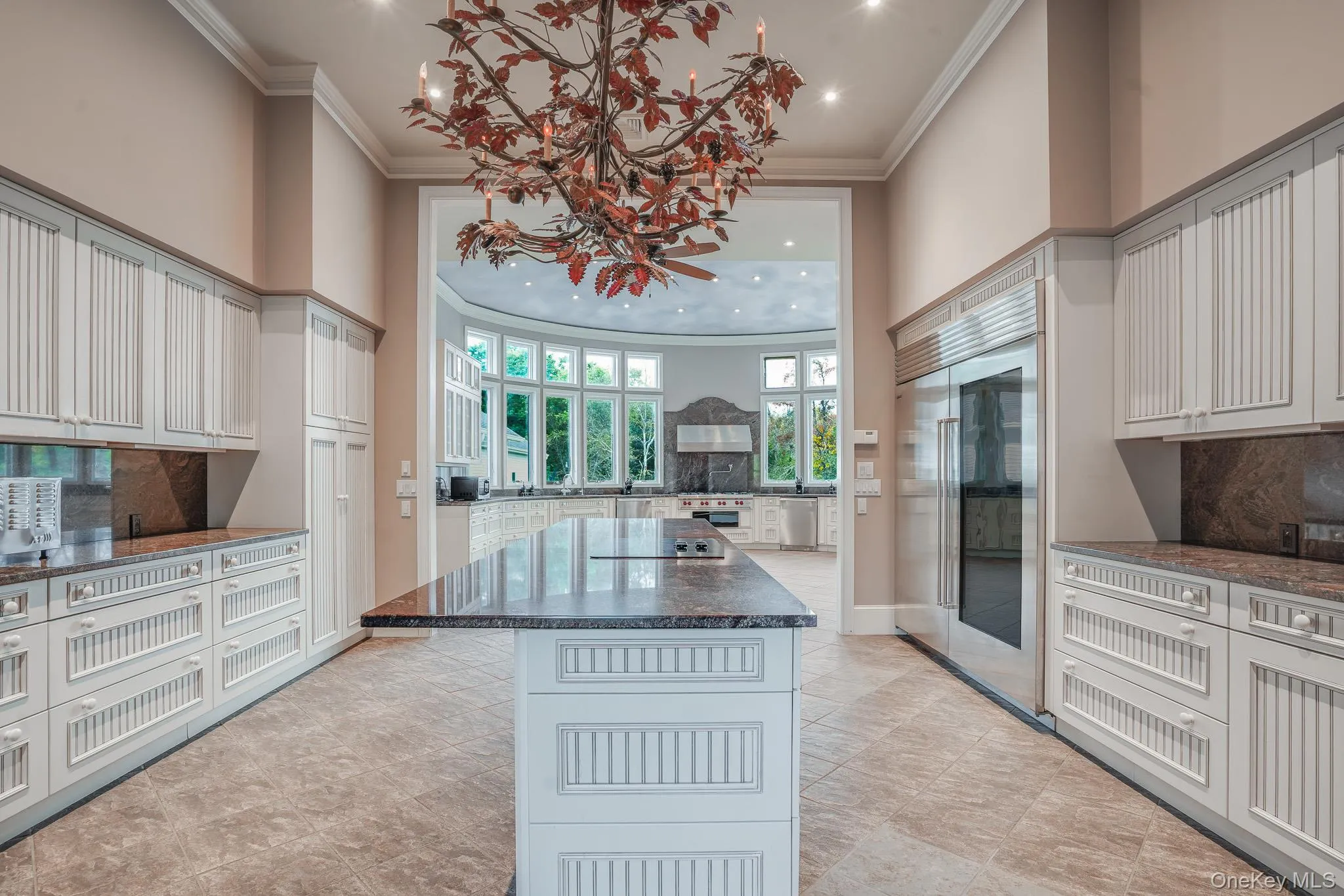 Spacious kitchen featuring white cabinetry, stone countertops, large center island with cooktop, and integrated stainless steel refrigerator. Spacious kitchen featuring white cabinetry, stone countertops, large center island with cooktop, and integrated stainless steel refrigerator.