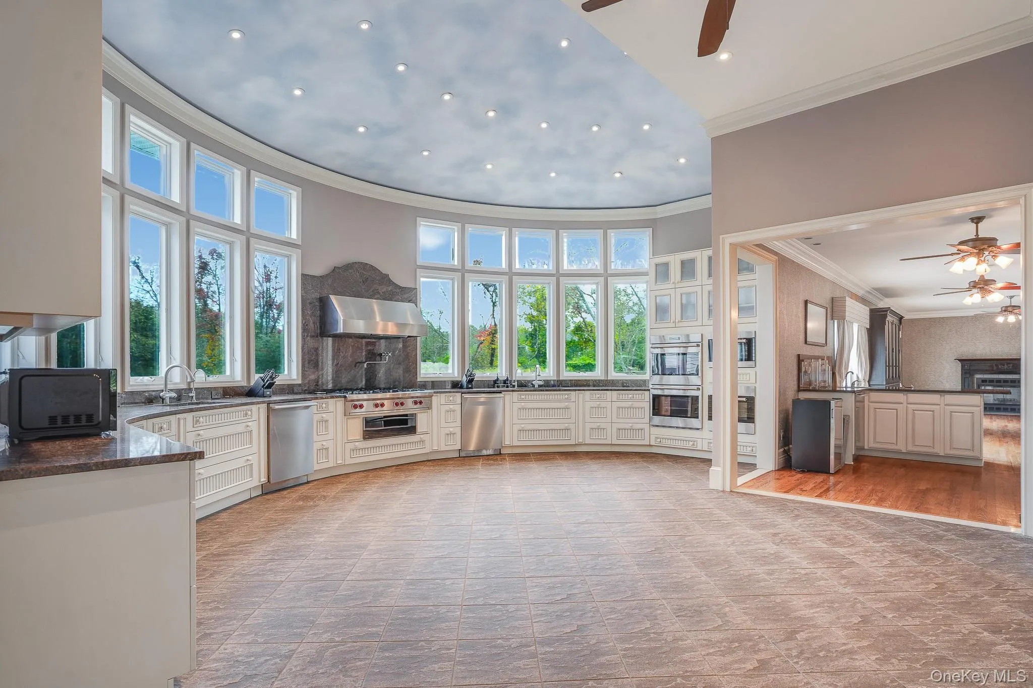 Curved chef's kitchen design featuring 20 foot windows on a rotunda wall, extensive white cabinetry, brown countertops, and stainless steel appliances. Curved chef's kitchen design featuring 20 foot windows on a rotunda wall, extensive white cabinetry, brown countertops, and stainless steel appliances.