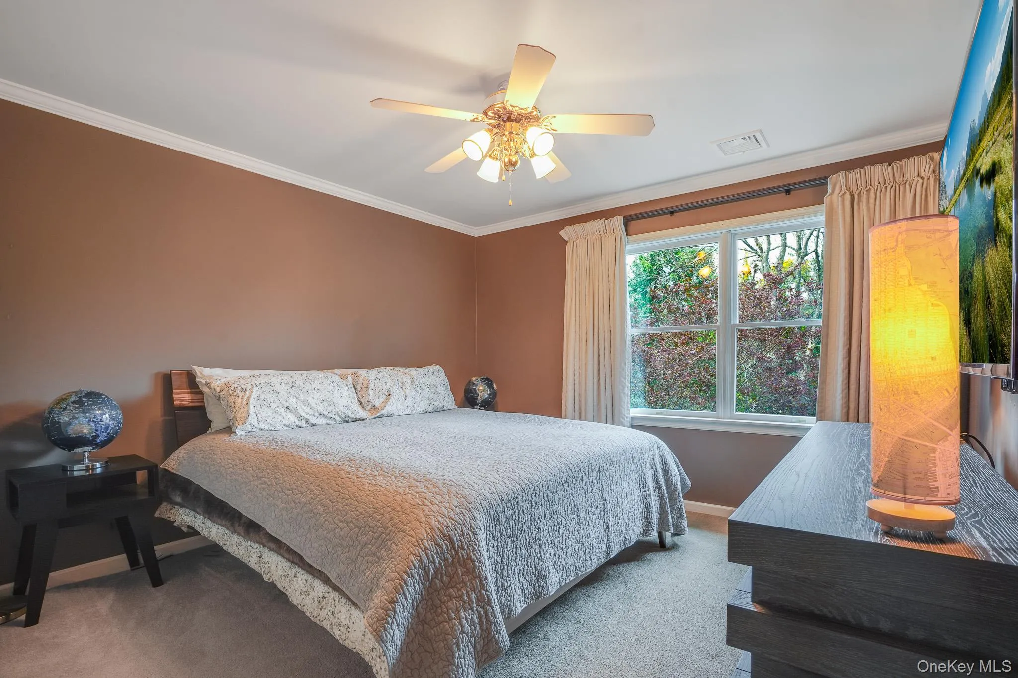 Bedroom with brown-toned walls with white crown molding, a ceiling fan with integrated lighting, a double window, and carpeted flooring. Bedroom with brown-toned walls with white crown molding, a ceiling fan with integrated lighting, a double window, and carpeted flooring.
