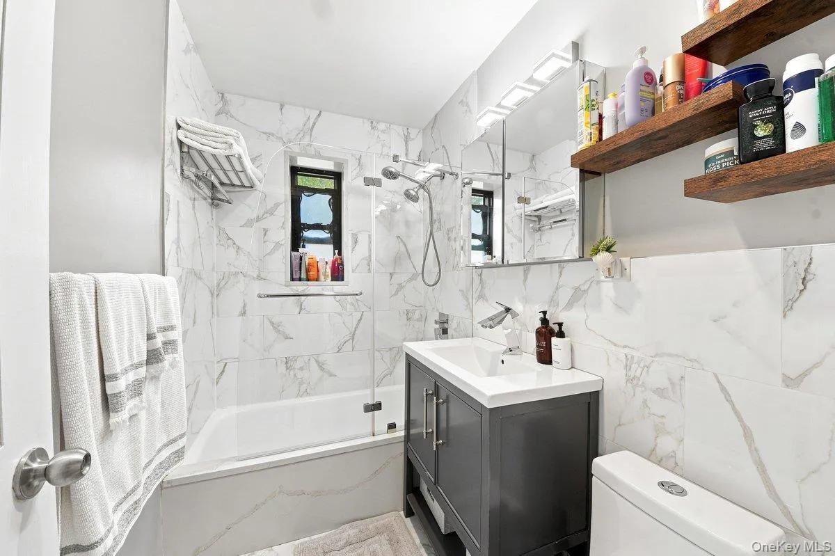 Updated bathroom featuring marble-patterned tile, modern vanity, glass shower enclosure, and excellent natural light Updated bathroom featuring marble-patterned tile, modern vanity, glass shower enclosure, and excellent natural light