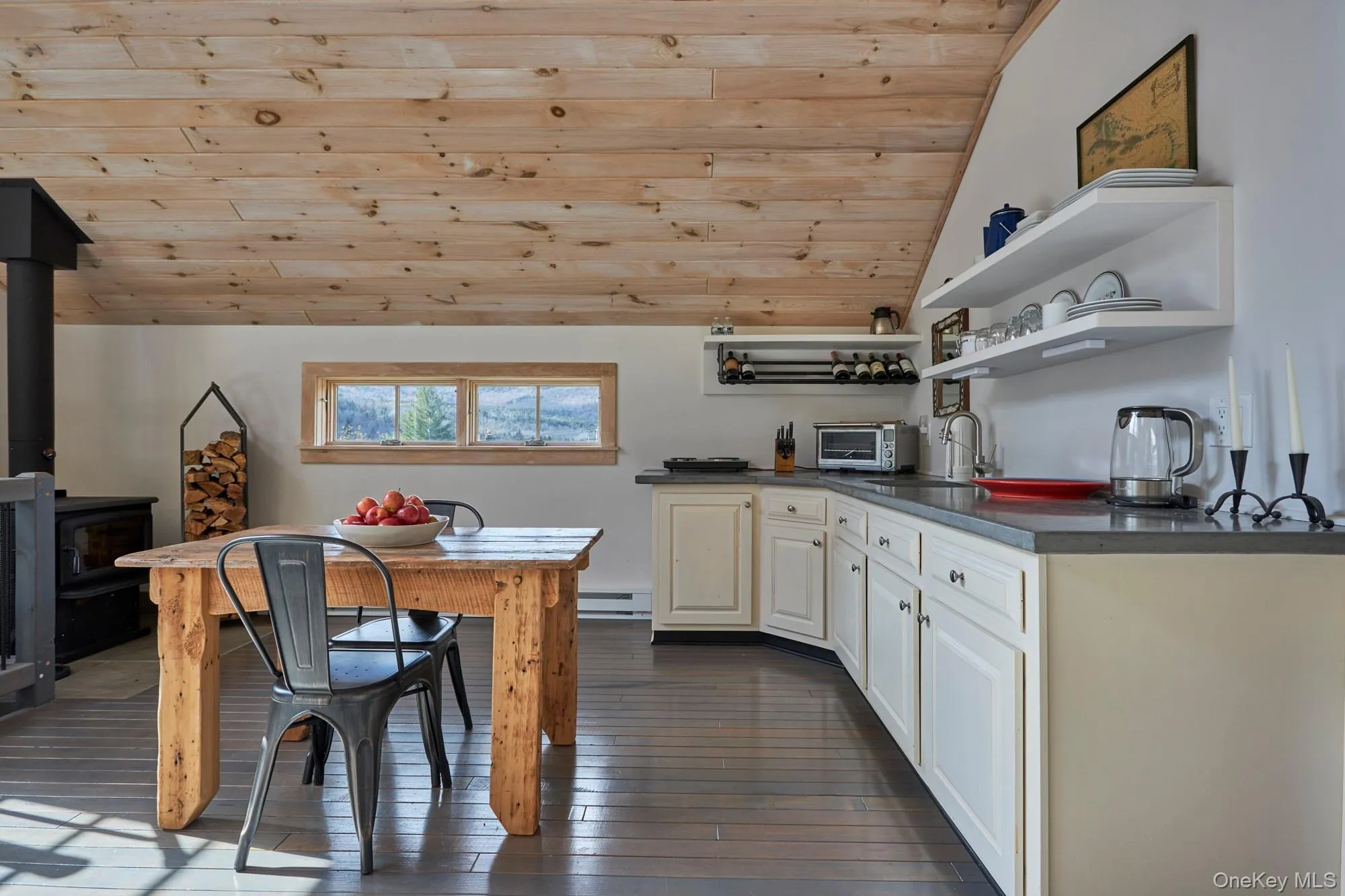 Kitchen with open shelves, dark countertops, lofted ceiling, a wood stove, and wood flooring. Kitchen with open shelves, dark countertops, lofted ceiling, a wood stove, and wood flooring.