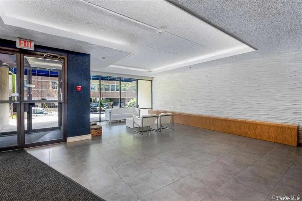 Expansive gray tile flooring, glass entry doors, full-height exterior windows, textured wall paneling, and a built-in wood-finish bench Expansive gray tile flooring, glass entry doors, full-height exterior windows, textured wall paneling, and a built-in wood-finish bench
