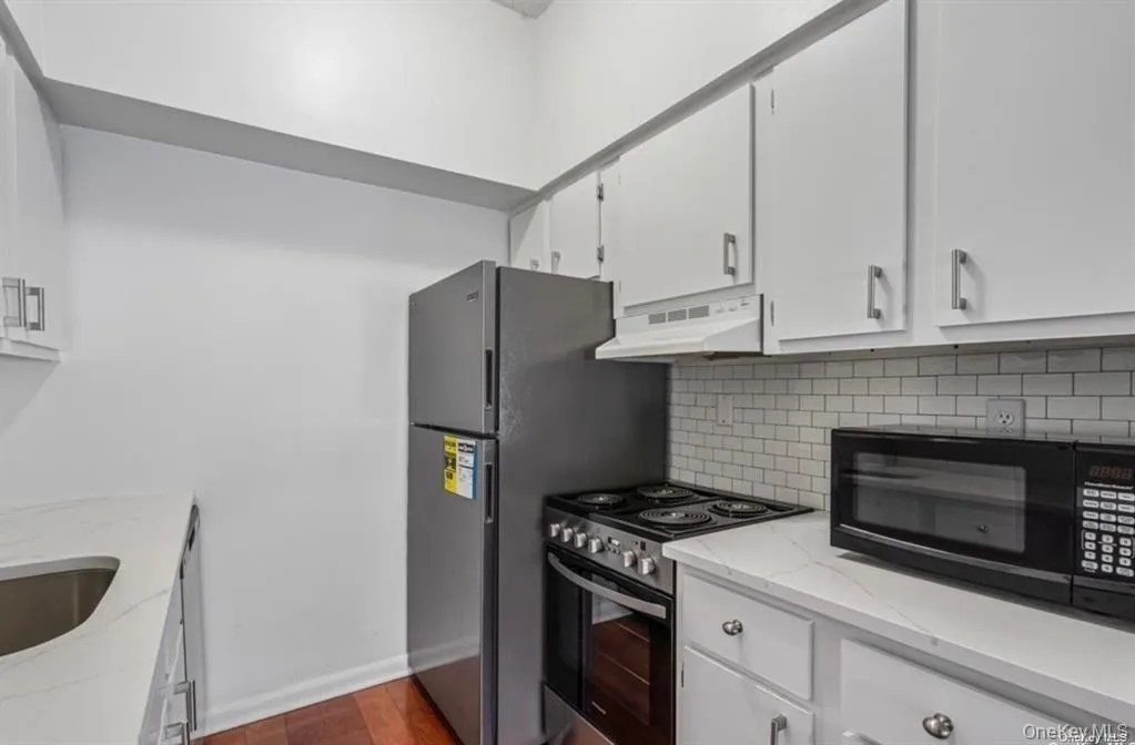 Kitchen featuring white cabinetry, white countertops, subway tile backsplash, and wood-finish flooring Kitchen featuring white cabinetry, white countertops, subway tile backsplash, and wood-finish flooring