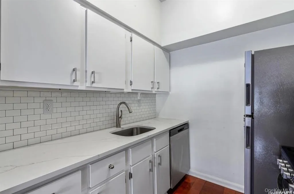 Updated kitchen featuring white cabinetry with brushed nickel hardware, white subway tile backsplash, stainless steel sink with single-handle faucet, quartz countertops, and stainless steel appliances including refrigerator and dishwasher Updated kitchen featuring white cabinetry with brushed nickel hardware, white subway tile backsplash, stainless steel sink with single-handle faucet, quartz countertops, and stainless steel appliances including refrigerator and dishwasher