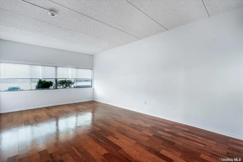 Rich wood-finish flooring, expansive windows with roller shades, bright white walls, and a textured ceiling Rich wood-finish flooring, expansive windows with roller shades, bright white walls, and a textured ceiling