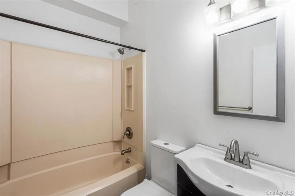 Tub-shower combination with integrated shelving, brushed nickel fixtures, wall-mounted mirror, and vanity with an integrated sink Tub-shower combination with integrated shelving, brushed nickel fixtures, wall-mounted mirror, and vanity with an integrated sink
