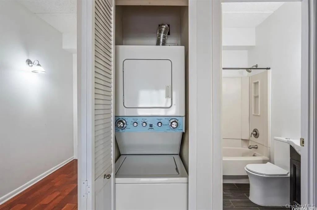 Stackable washer and dryer, louvered bi-fold doors, wall-mounted light fixture, wood-finish flooring, white wall paint Stackable washer and dryer, louvered bi-fold doors, wall-mounted light fixture, wood-finish flooring, white wall paint