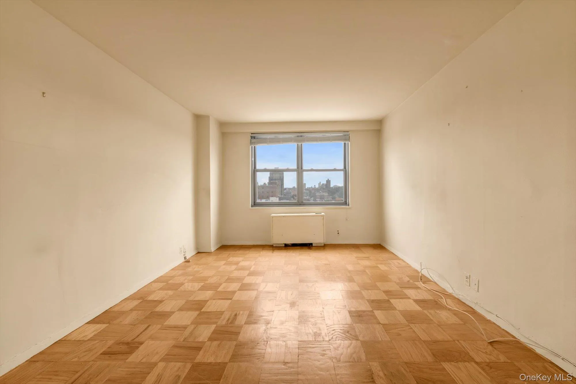 Parquet wood-finish flooring, neutral wall tones, window with a cityscape backdrop, and a built-in heating/cooling unit Parquet wood-finish flooring, neutral wall tones, window with a cityscape backdrop, and a built-in heating/cooling unit