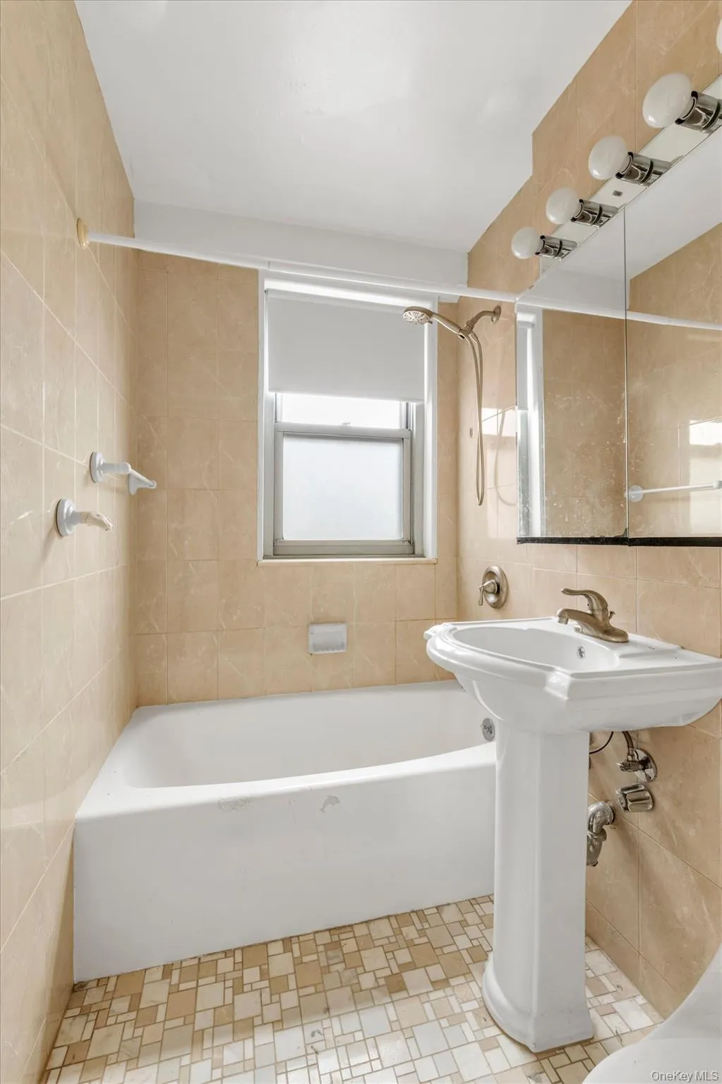 Full bathroom featuring a pedestal sink, white bathtub, wall-mounted showerhead with hose, and mosaic tile flooring Full bathroom featuring a pedestal sink, white bathtub, wall-mounted showerhead with hose, and mosaic tile flooring
