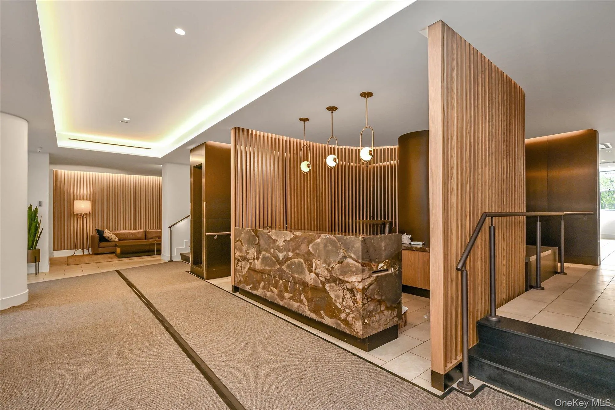 Reception area featuring a stone-clad desk, wood-slat wall accents, contemporary pendant lighting, and recessed ceiling lighting Reception area featuring a stone-clad desk, wood-slat wall accents, contemporary pendant lighting, and recessed ceiling lighting