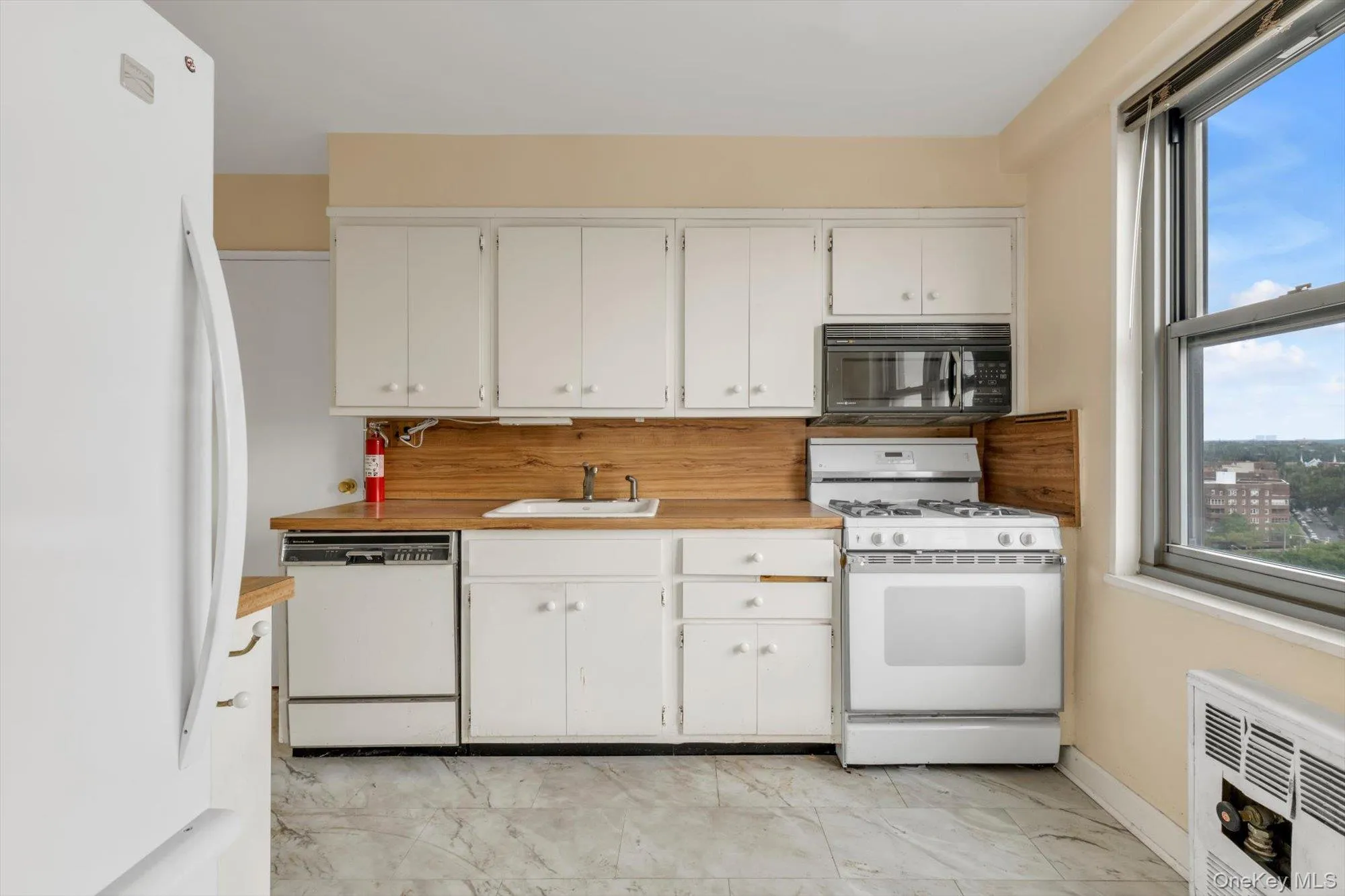 Kitchen featuring white cabinetry, wood-finish countertops, white appliances, and a window with urban scenery Kitchen featuring white cabinetry, wood-finish countertops, white appliances, and a window with urban scenery