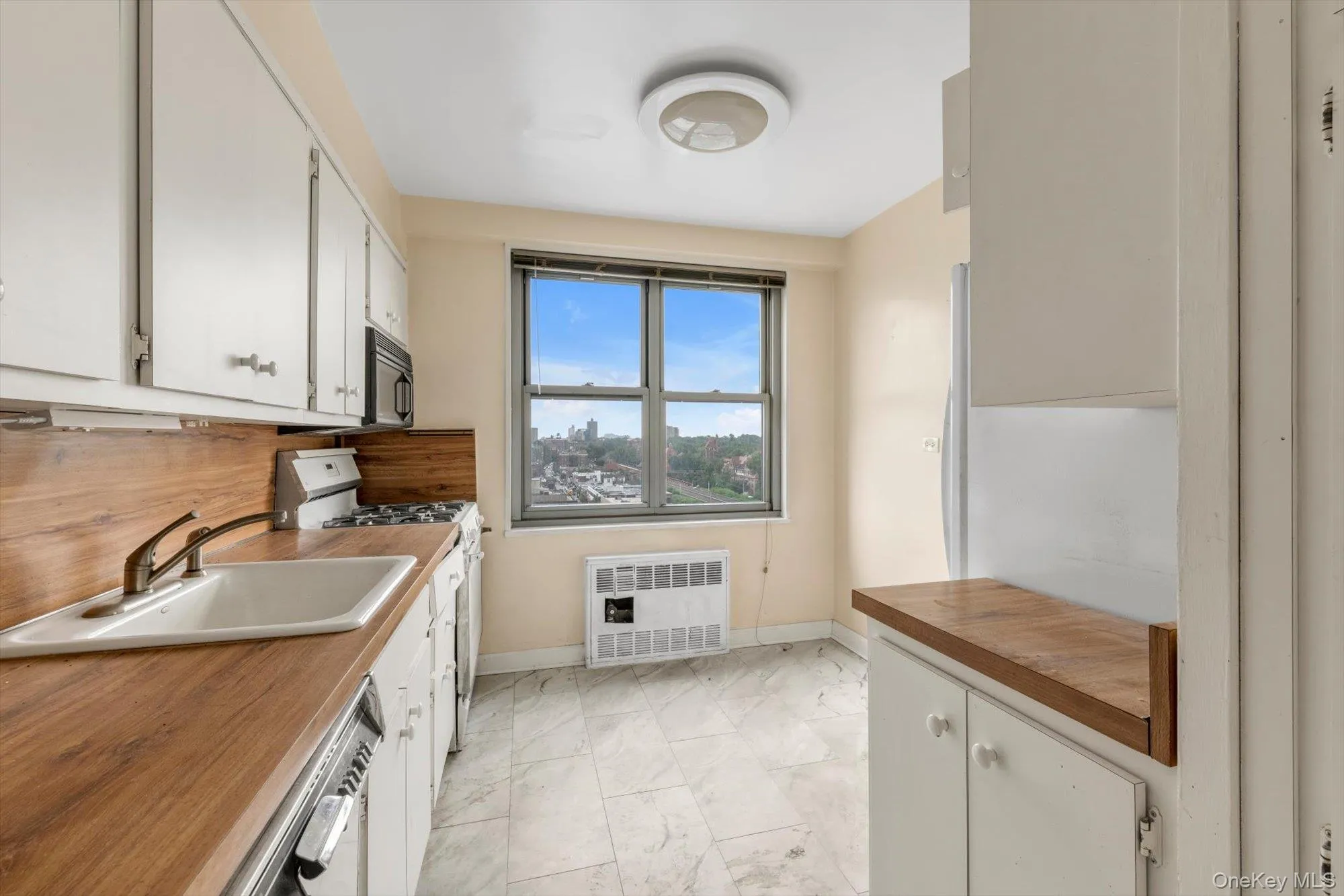 Kitchen featuring white cabinetry, wood-finish countertops, stainless steel sink, and a large window Kitchen featuring white cabinetry, wood-finish countertops, stainless steel sink, and a large window