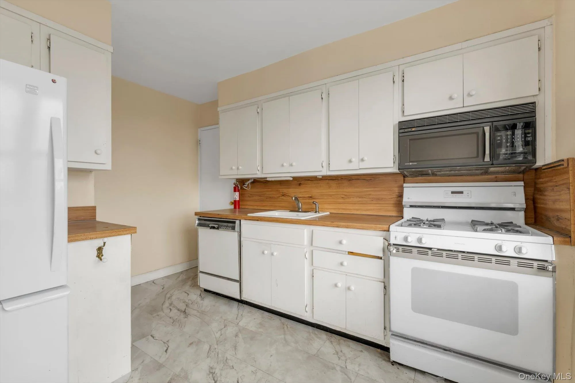 Kitchen featuring white cabinetry, wood-finish countertops, stainless steel sink, and white appliances including a refrigerator, dishwasher, and range with an overhead microwave Kitchen featuring white cabinetry, wood-finish countertops, stainless steel sink, and white appliances including a refrigerator, dishwasher, and range with an overhead microwave