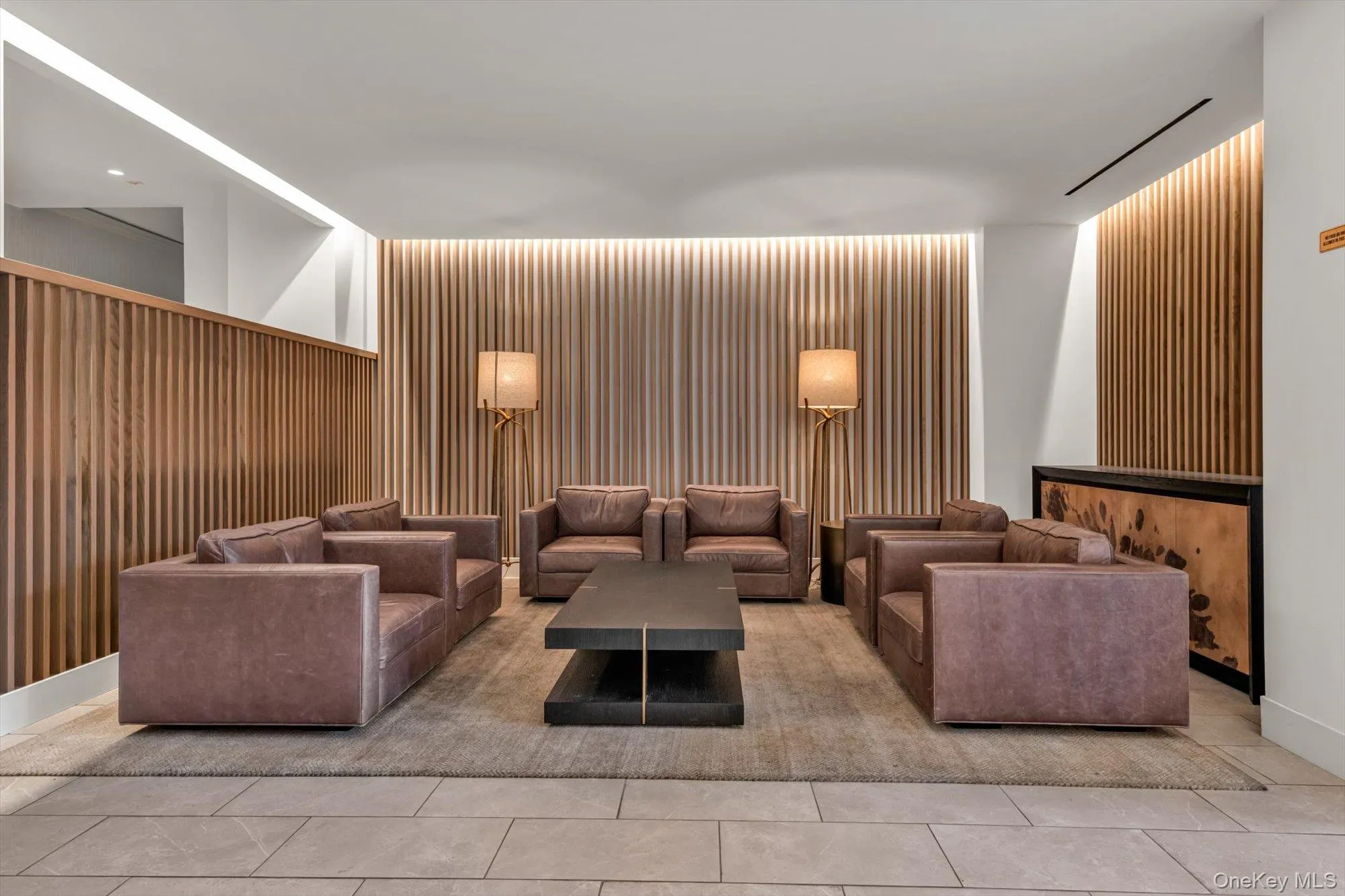 Contemporary lounge area with slat wood wall paneling, recessed lighting, and tile flooring Contemporary lounge area with slat wood wall paneling, recessed lighting, and tile flooring