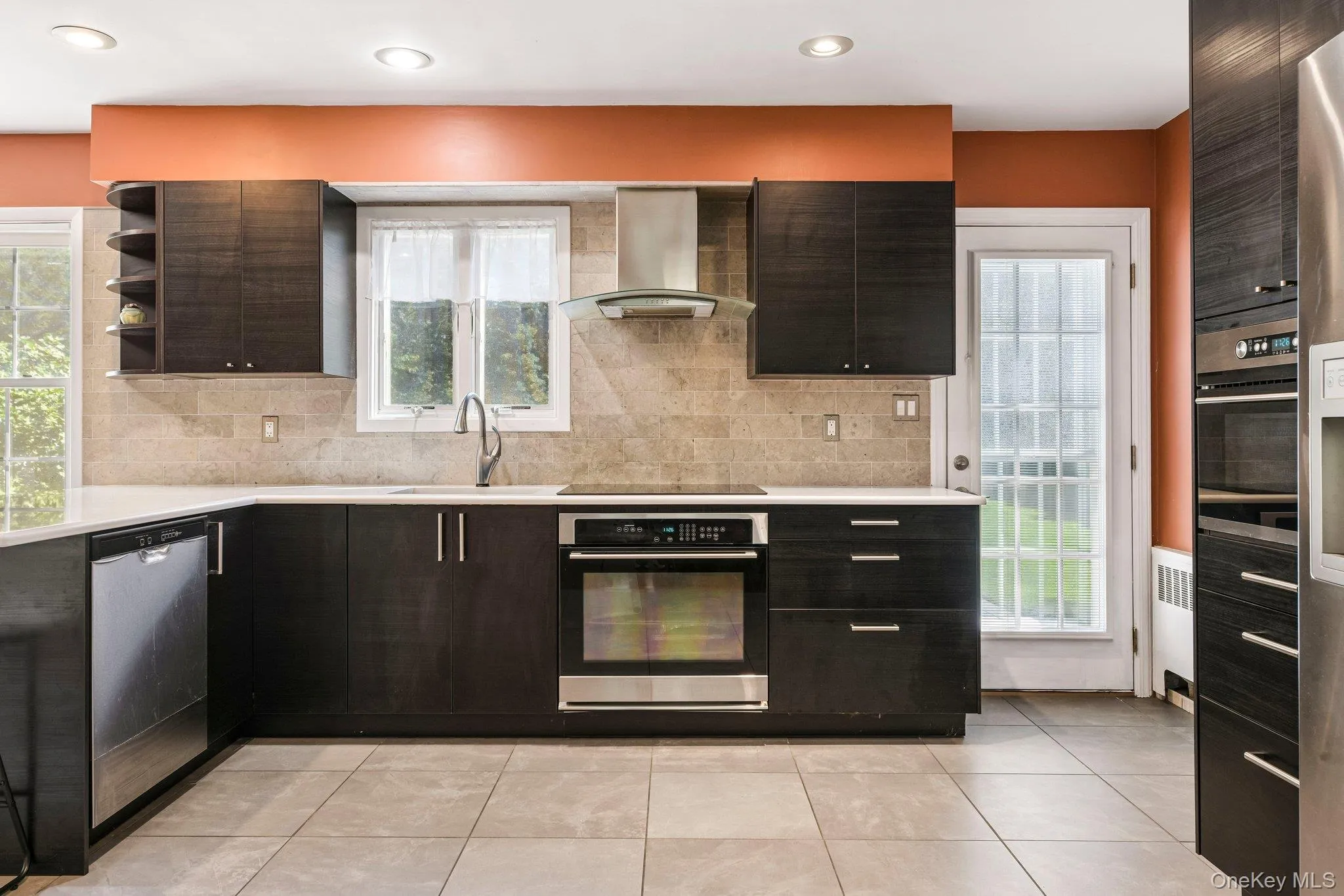 Kitchen view from dining room. High hat lighting, modern exhaust cooking fan, stainless steel appliances, built in wall microwave, tiled floor and quartz counter top with beautiful sink window view of yard. Kitchen view from dining room. High hat lighting, modern exhaust cooking fan, stainless steel appliances, built in wall microwave, tiled floor and quartz counter top with beautiful sink window view of yard.