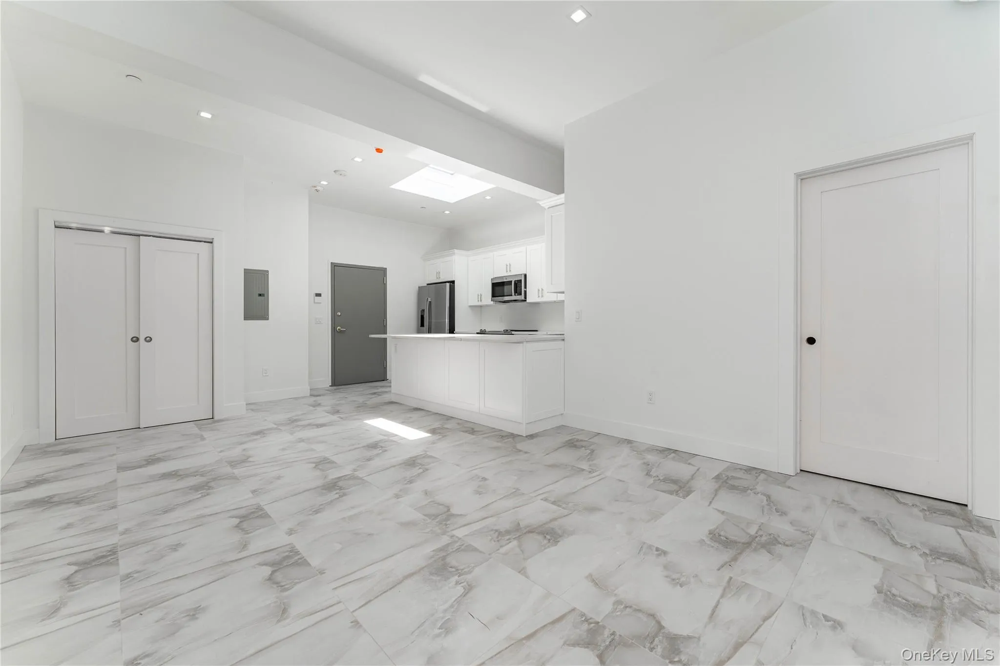 Unfurnished living room with recessed lighting, light marble finish flooring, electric panel, baseboards, and a towering ceiling Unfurnished living room with recessed lighting, light marble finish flooring, electric panel, baseboards, and a towering ceiling