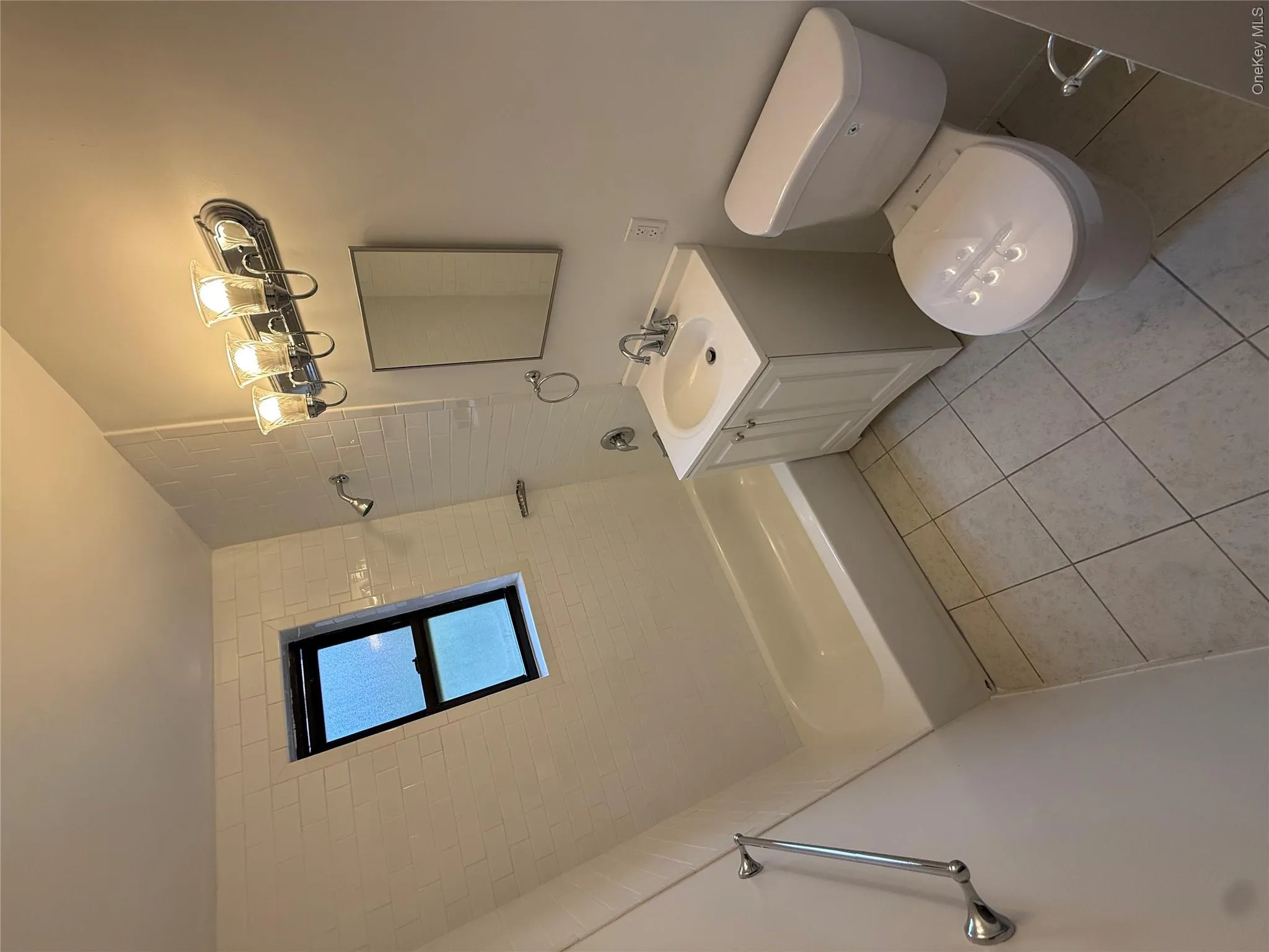 Full bathroom featuring a white vanity with integrated sink, white tiled walls, and a white bathtub with a shower fixture Full bathroom featuring a white vanity with integrated sink, white tiled walls, and a white bathtub with a shower fixture