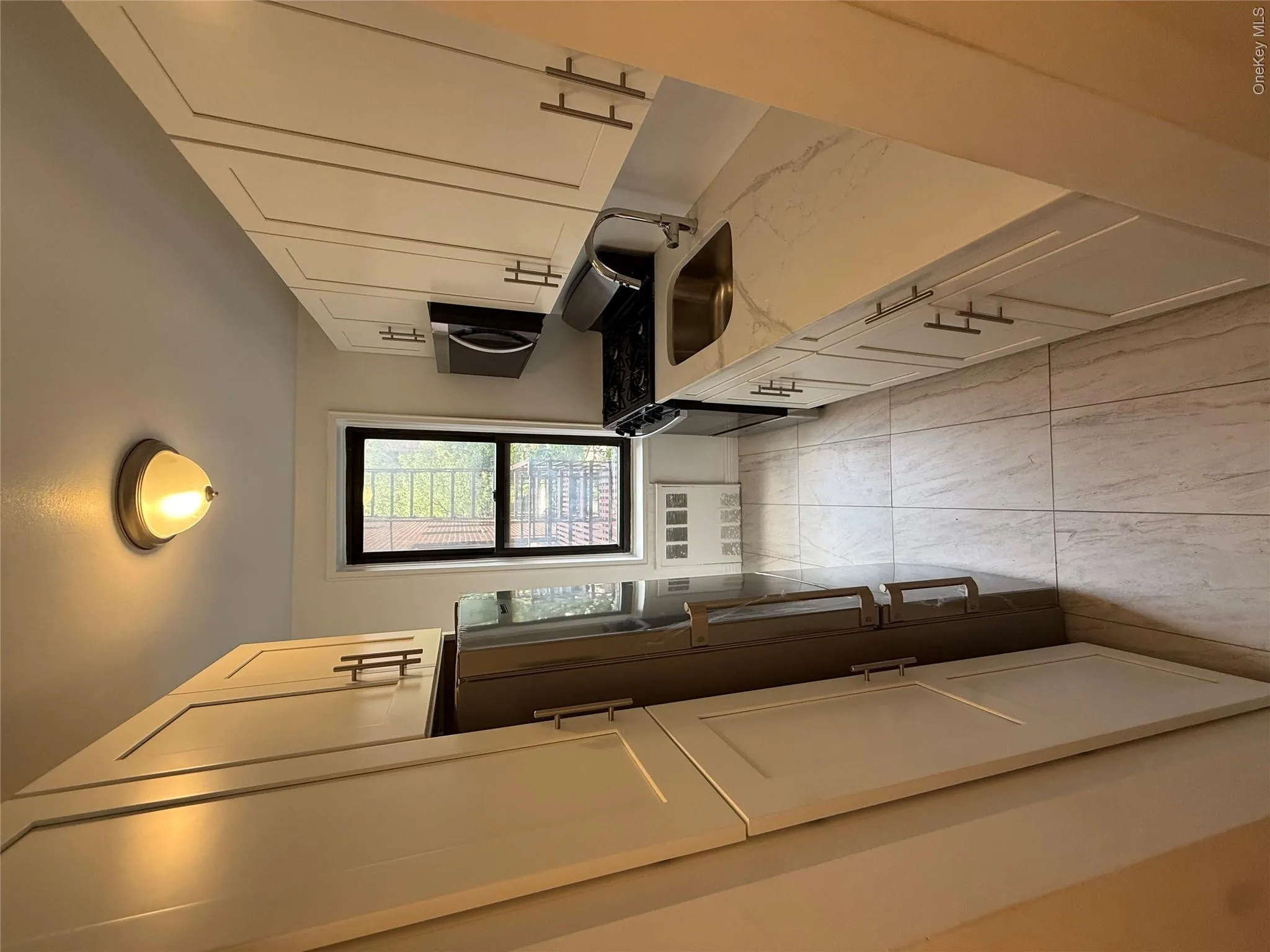 Galley kitchen featuring white shaker cabinetry, stainless steel appliances, stone-look countertops, and tile flooring Galley kitchen featuring white shaker cabinetry, stainless steel appliances, stone-look countertops, and tile flooring