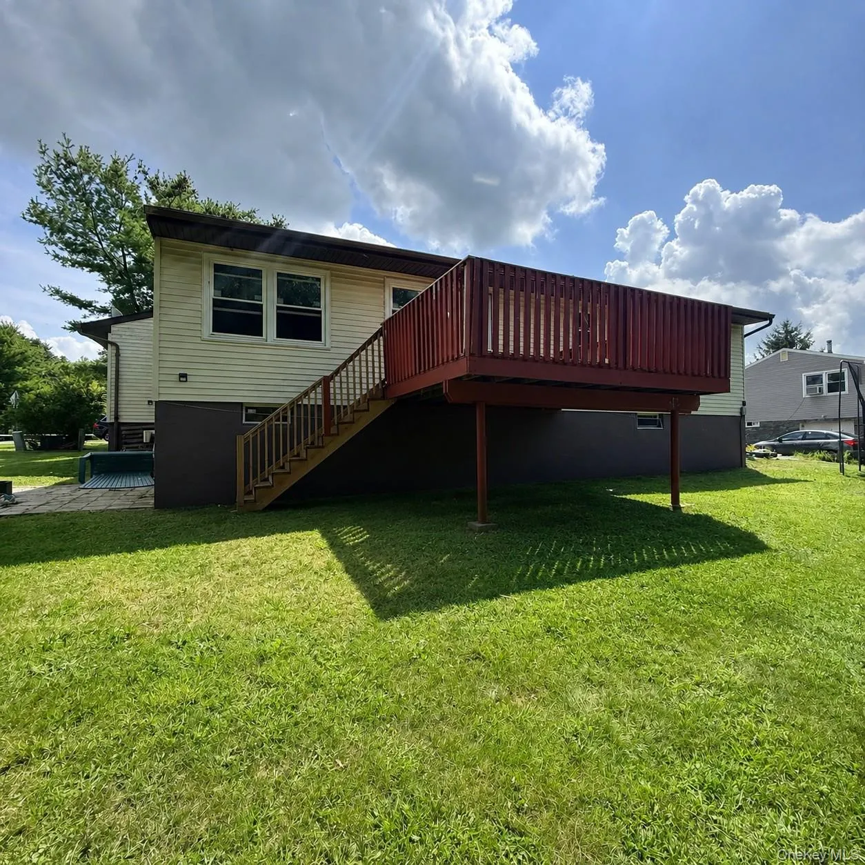 Expansive lawn with a two-story residence, featuring a raised deck with wood railings and a staircase Expansive lawn with a two-story residence, featuring a raised deck with wood railings and a staircase