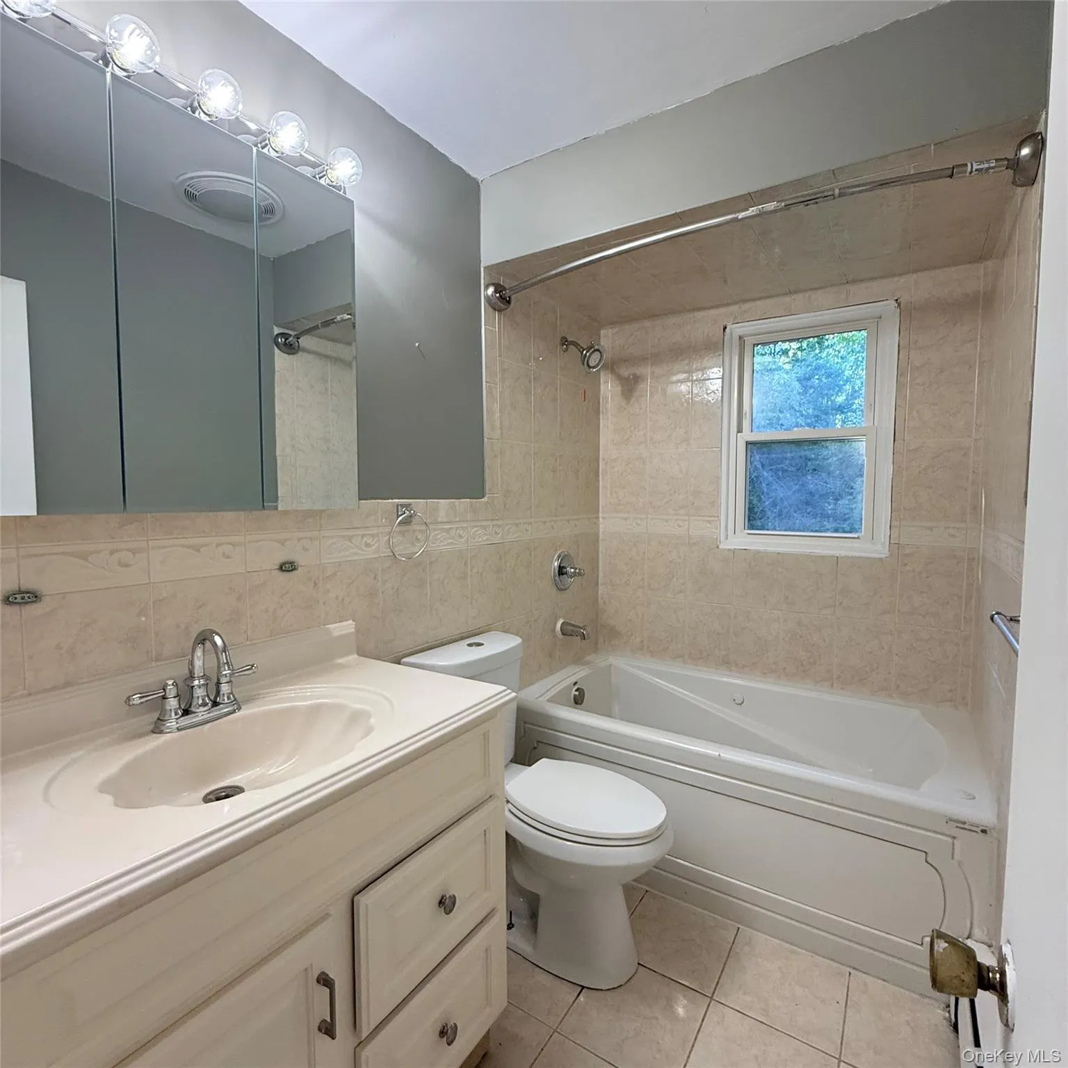 Full bathroom featuring a vanity with integrated sink, chrome fixtures, tile flooring, and a jetted tub with tiled surround Full bathroom featuring a vanity with integrated sink, chrome fixtures, tile flooring, and a jetted tub with tiled surround
